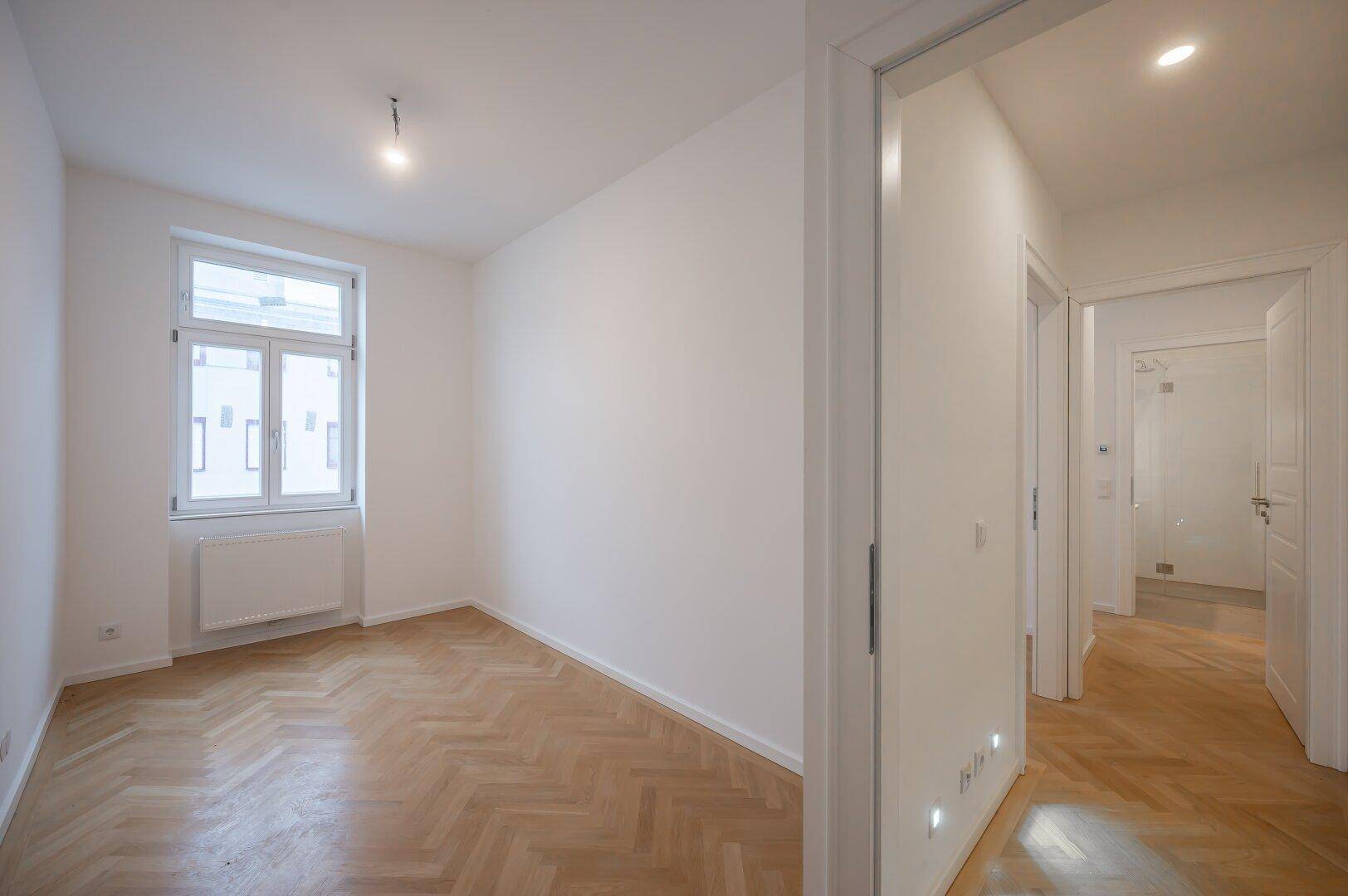 Heller Flur mit Fischgrätparkett und Zugang zu weiteren Zimmern und einem Badezimmer.