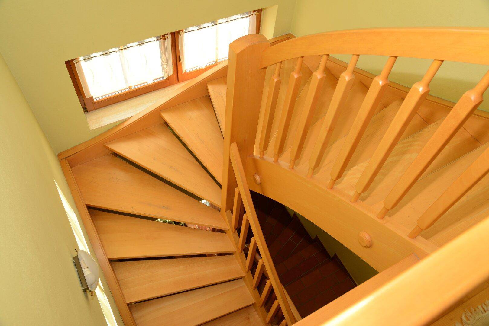 Elegante Holztreppe mit geschwungenem Geländer, die die verschiedenen Ebenen verbindet.
