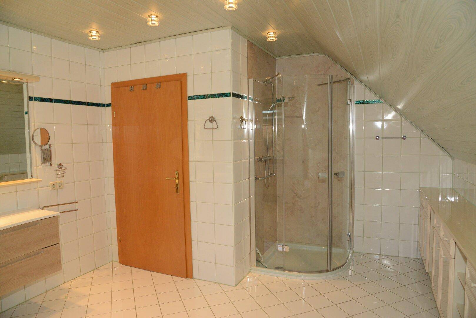 Geräumiges Badezimmer mit Duschkabine, weißen Fliesen und Dachschräge.