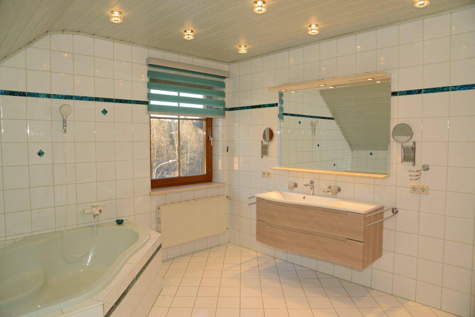 Helles Badezimmer mit Badewanne, Waschtisch und Fenster, gefliest in Weiß und Türkis.