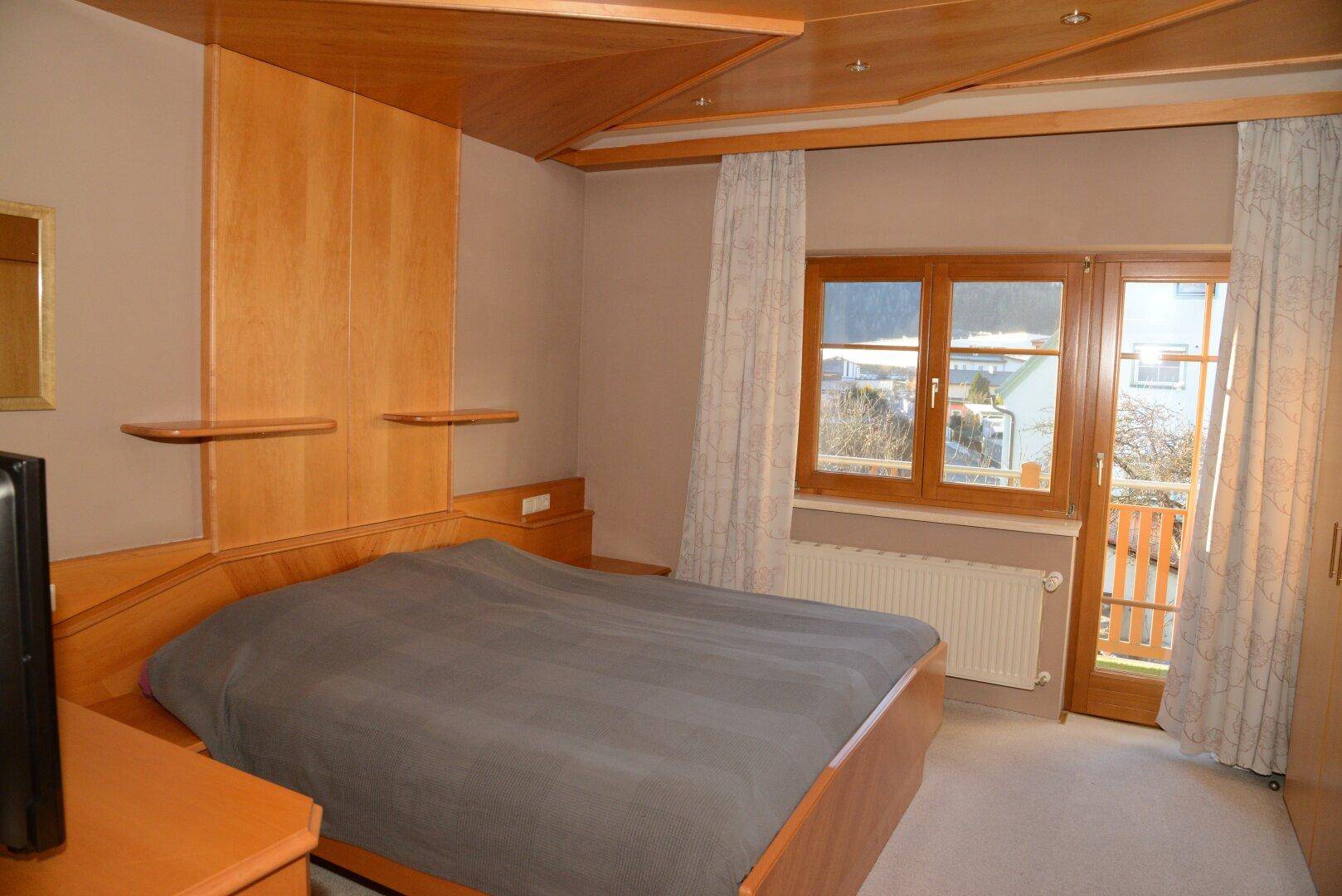 Gemütliches Schlafzimmer mit Holzbett, Teppichboden und Zugang zum Balkon.