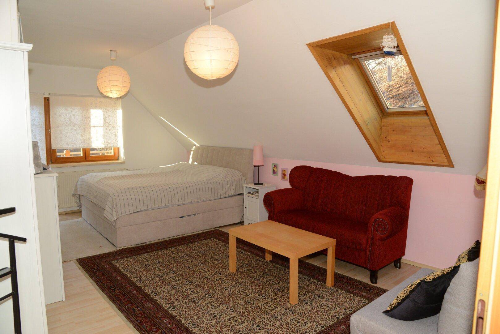 Helles Schlafzimmer im Dachgeschoss mit Bett, Sofa und Dachfenster.
