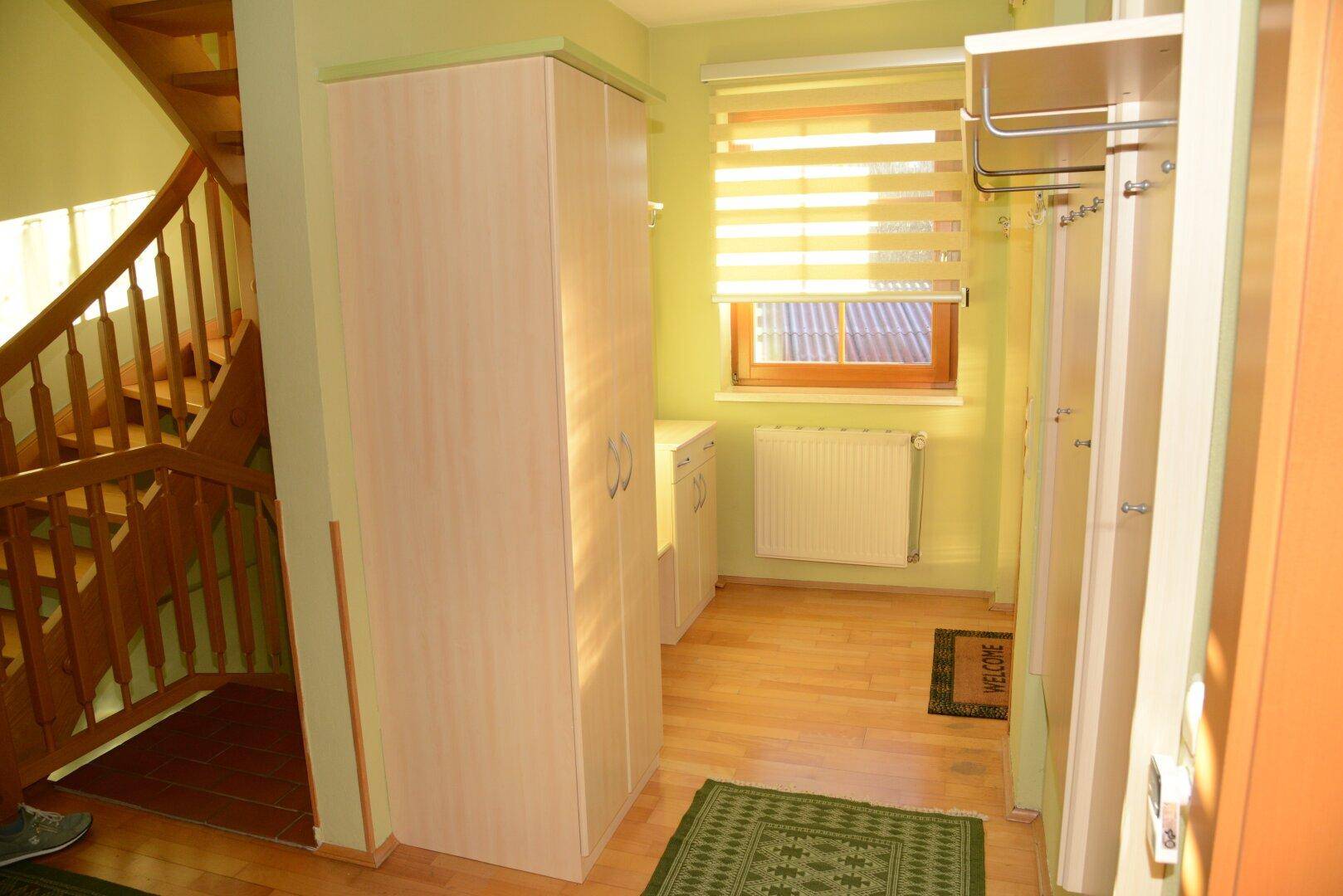 Heller Eingangsbereich mit Garderobe, Schränken und Holztreppe.