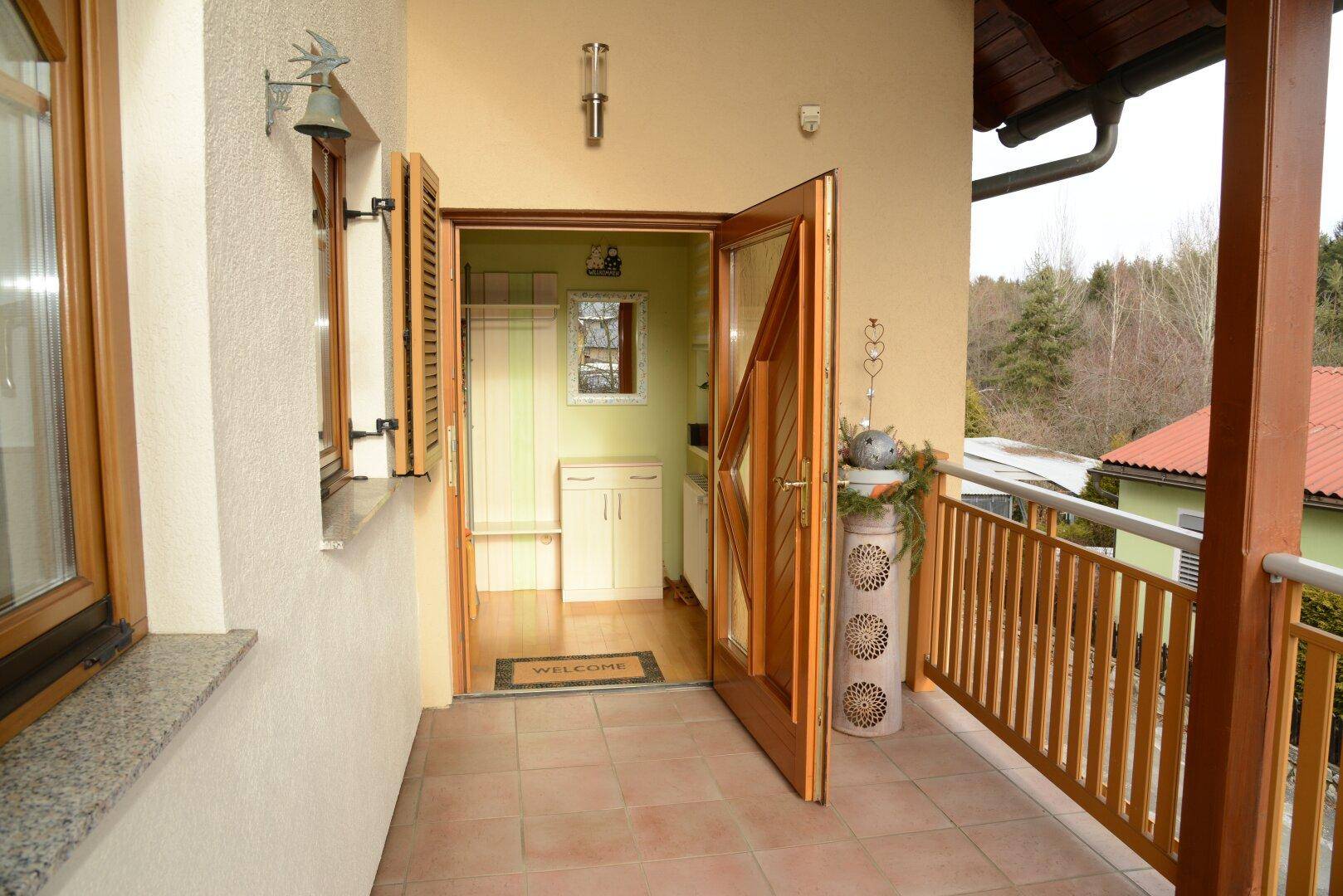 Gefliester Balkon mit Holzgeländer und Zugang zu einem hellen Innenraum.