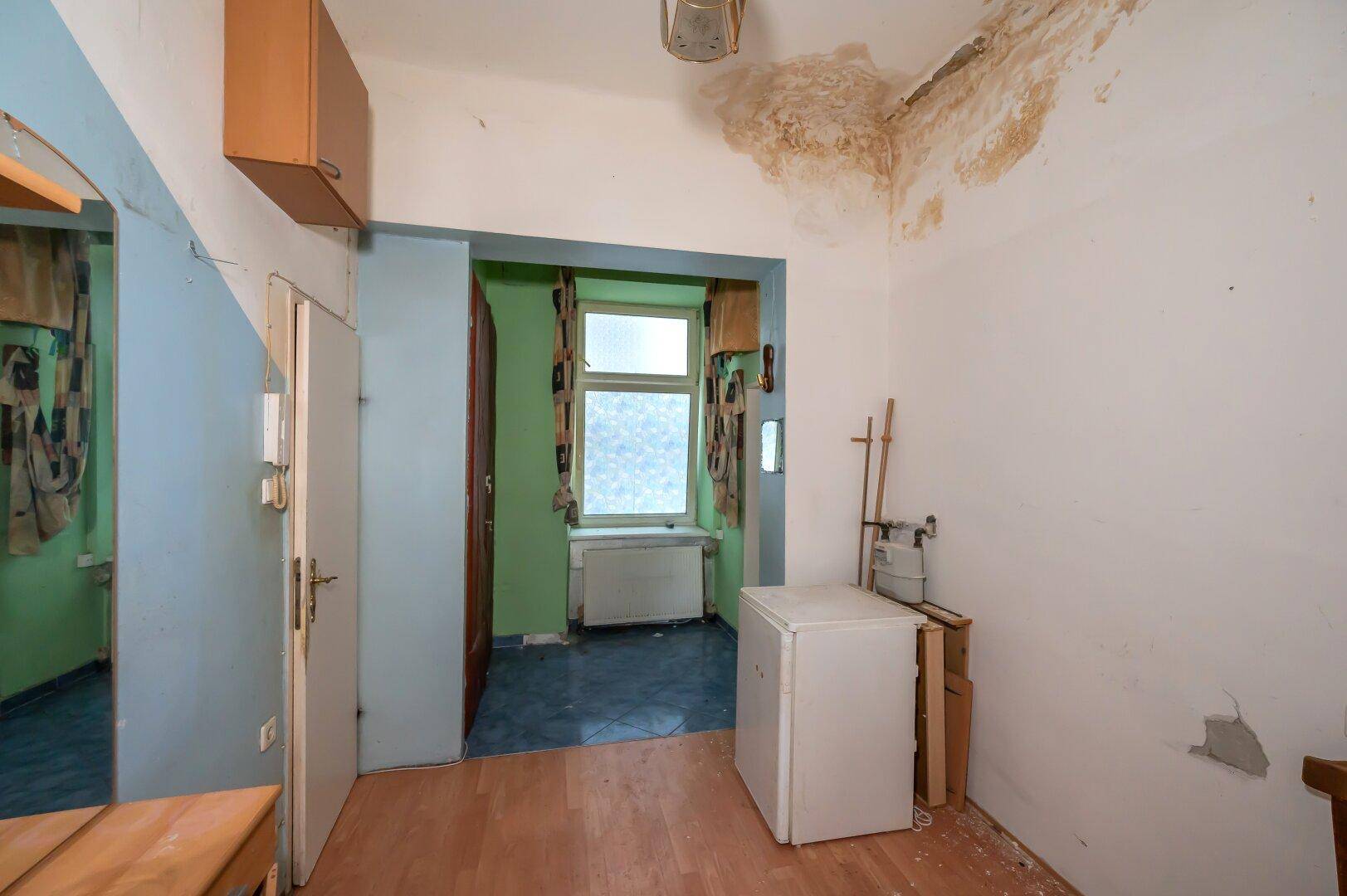 Flur mit Laminatboden, Kühlschrank und Blick in ein weiteres Zimmer, zeigt Renovierungsbedarf.