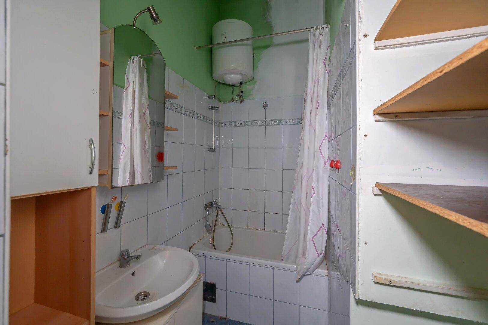 Badezimmer mit Badewanne, Waschbecken und Boiler, zeigt deutlichen Renovierungsbedarf.
