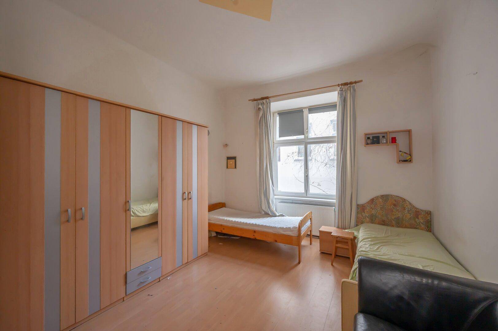 Schlafzimmer mit zwei Einzelbetten, großem Kleiderschrank und Laminatboden, bereit zur Modernisierung.