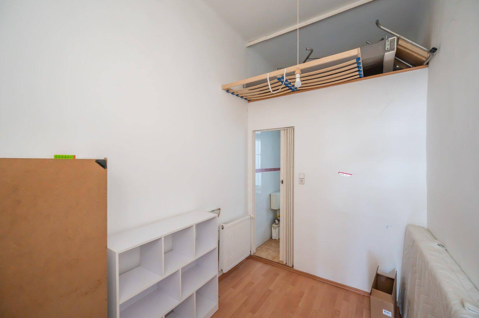 Kleines Zimmer mit Laminatboden, Regal und erhöhtem Stauraum, mit Zugang zu einem Bad.