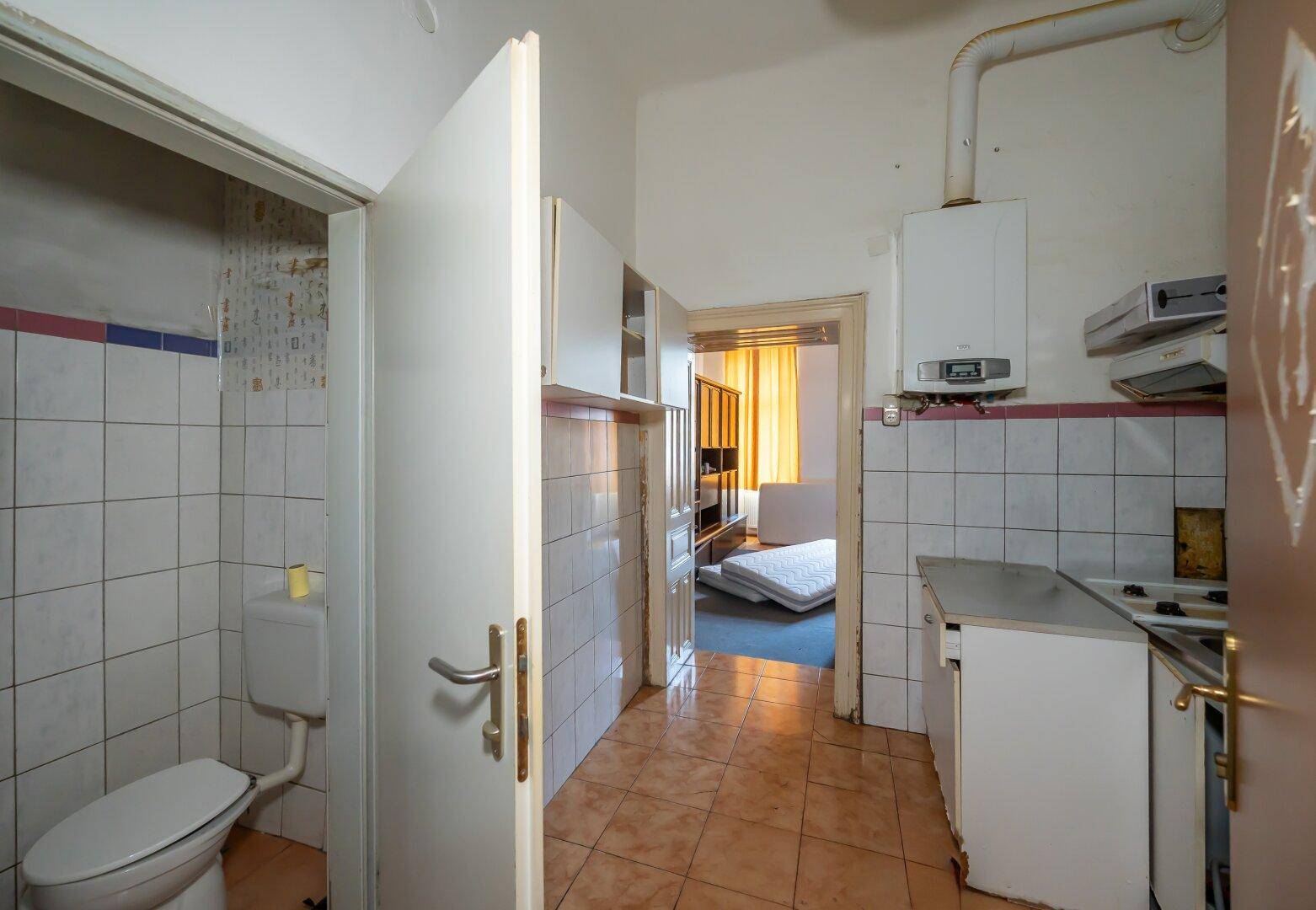 Küche mit Fliesenboden, Gastherme und integrierter Toilette, die eine Renovierung benötigt.