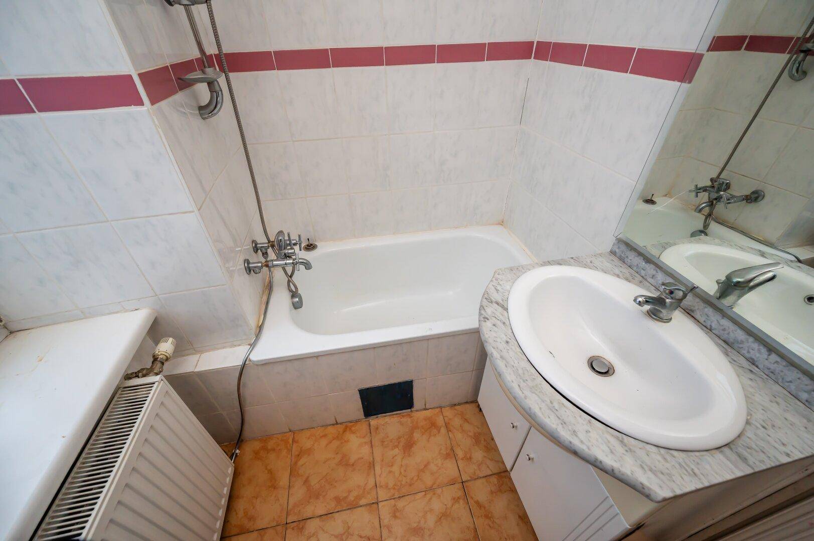 Badezimmer mit Badewanne, Waschbecken und Spiegel, gefliest.