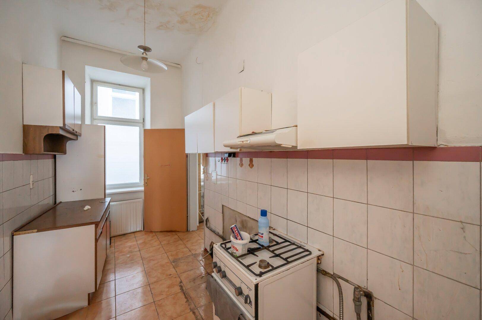Küche mit Gasherd, Hängeschränken und Fenster, die eine Renovierung benötigt.