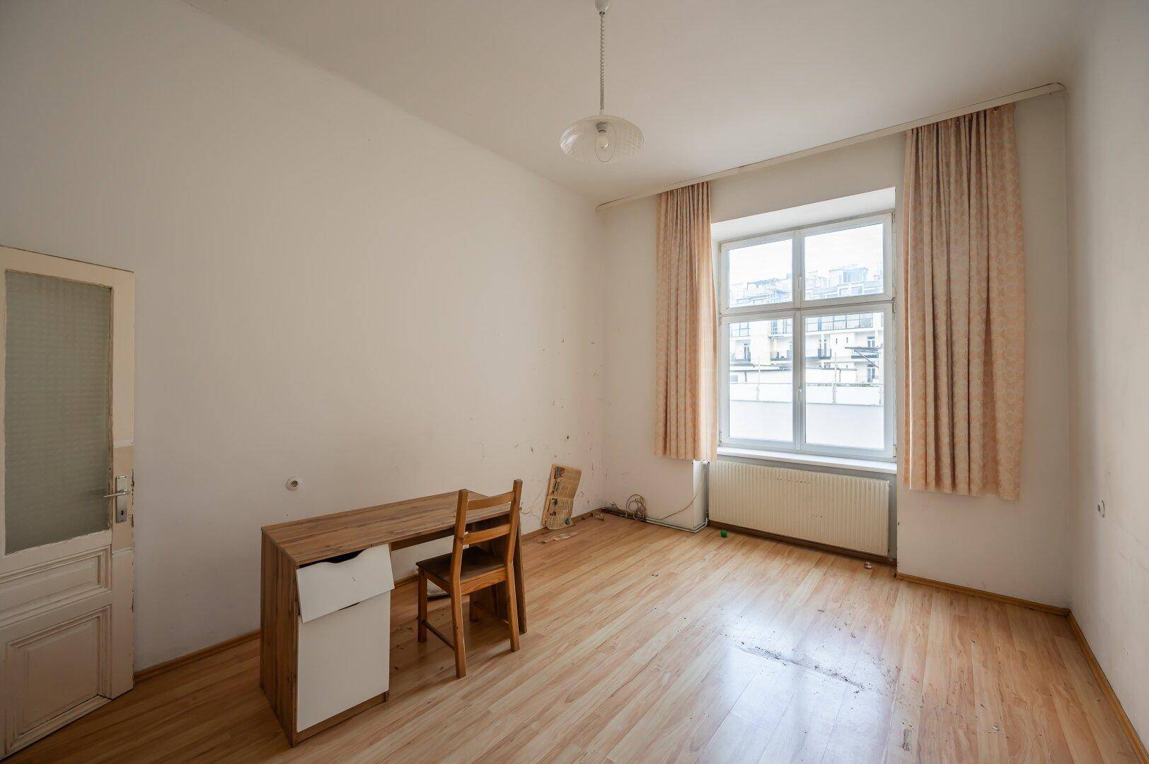 Helles Zimmer mit Laminatboden, einem Schreibtisch und Fenster mit Blick nach draußen.