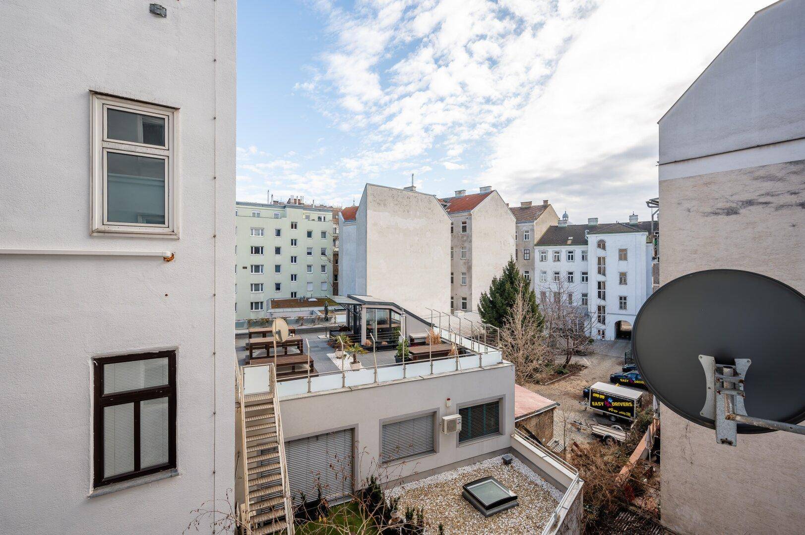 Dachterrasse mit Sitzgelegenheiten und Blick auf umliegende Gebäude und den Innenhof.