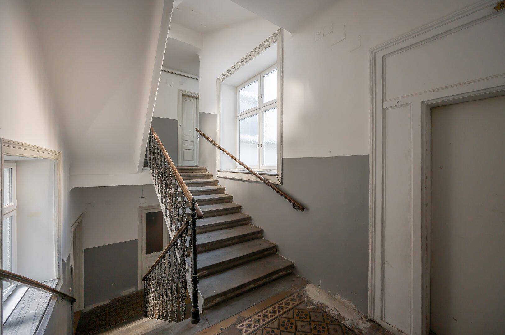 Geräumiges Treppenhaus mit großen Fenstern und klassischem Geländer in einem Altbau.