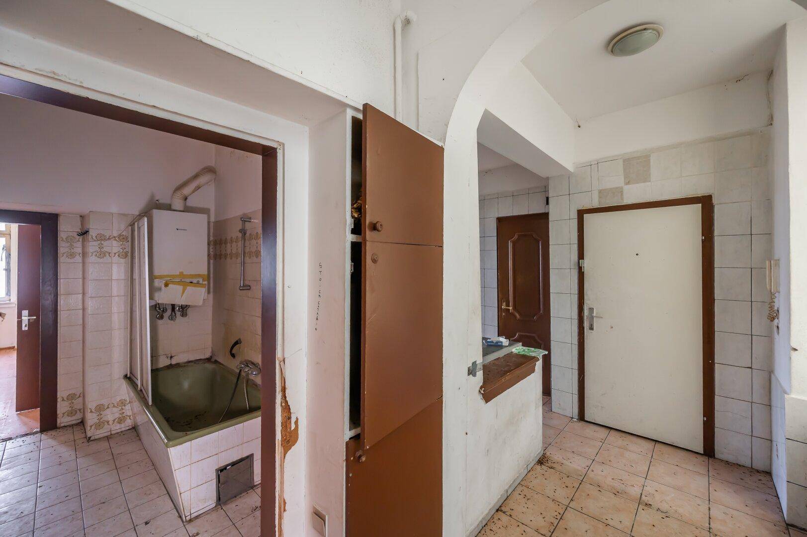 Altes Badezimmer mit grüner Badewanne, Fliesen und einem Warmwasserbereiter, renovierungsbedürftig.
