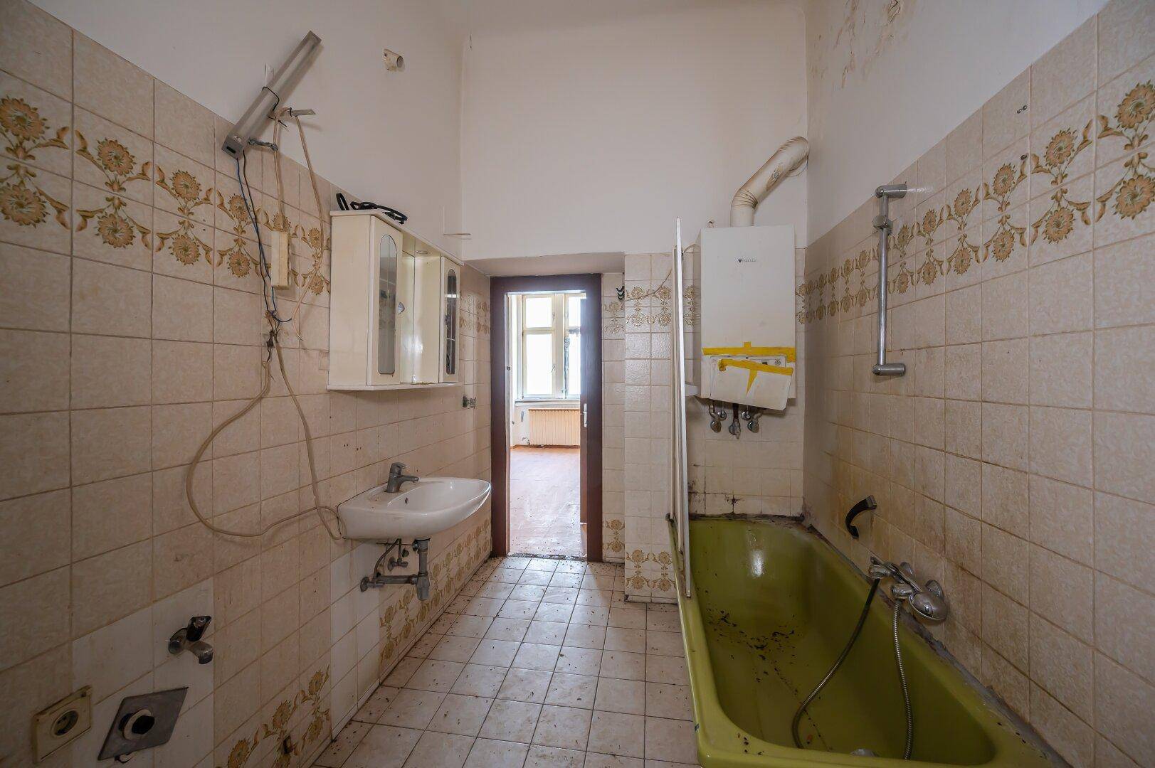 Veraltetes Badezimmer mit grüner Badewanne, Waschbecken und Fliesen, das eine Modernisierung benötigt.