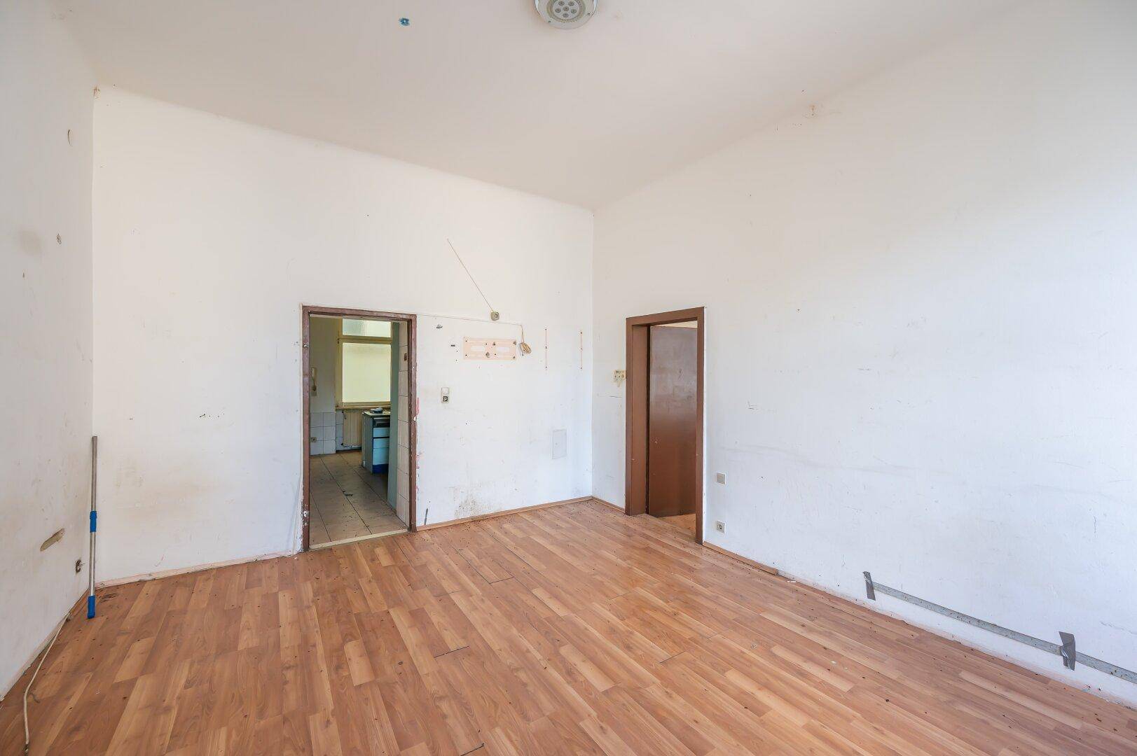 Leeres Zimmer mit Holzboden und zwei Türen, das auf eine bevorstehende Renovierung wartet.