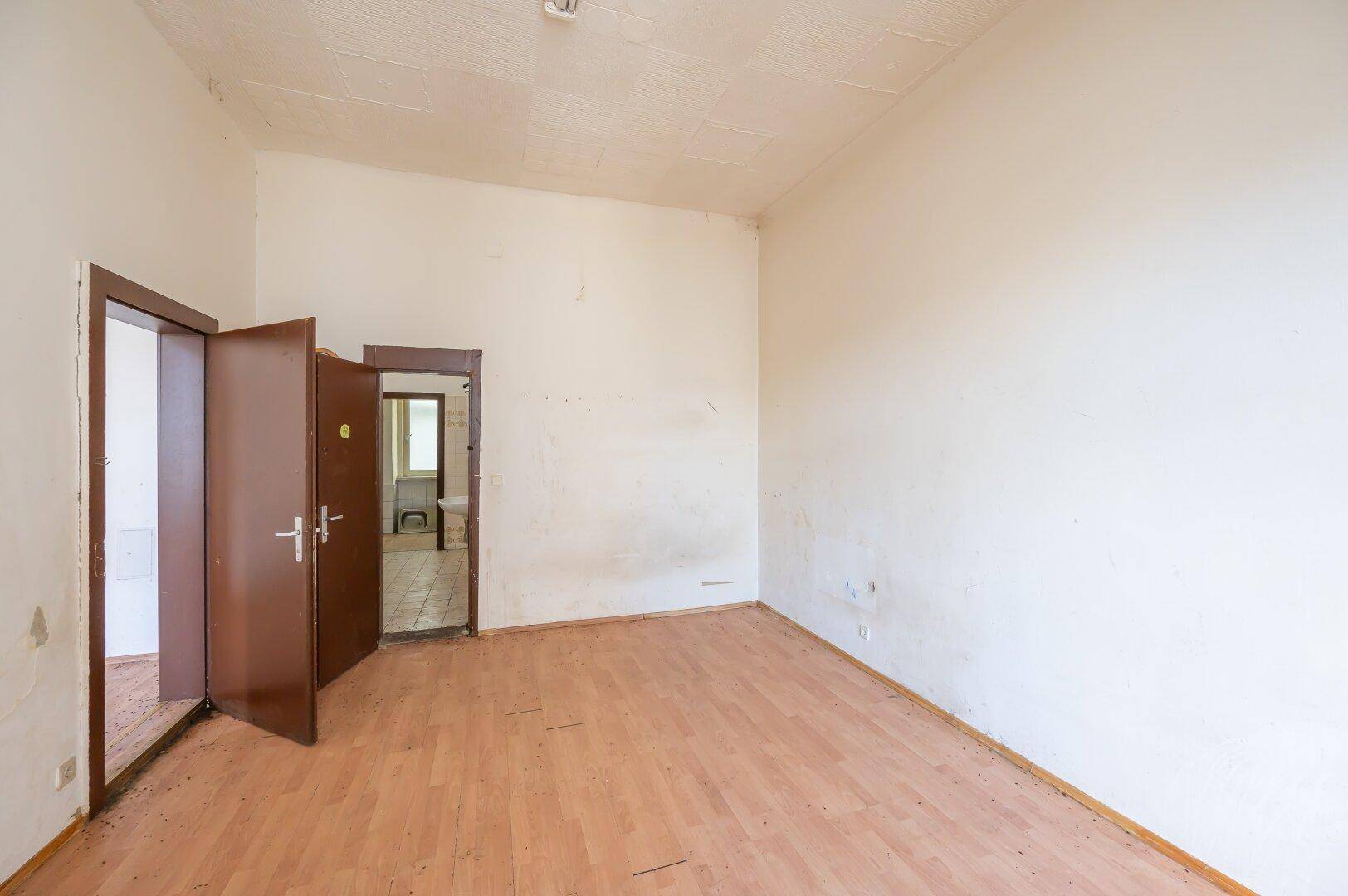 Leeres Zimmer mit Holzboden und mehreren Türen, das Renovierungsarbeiten erfordert.