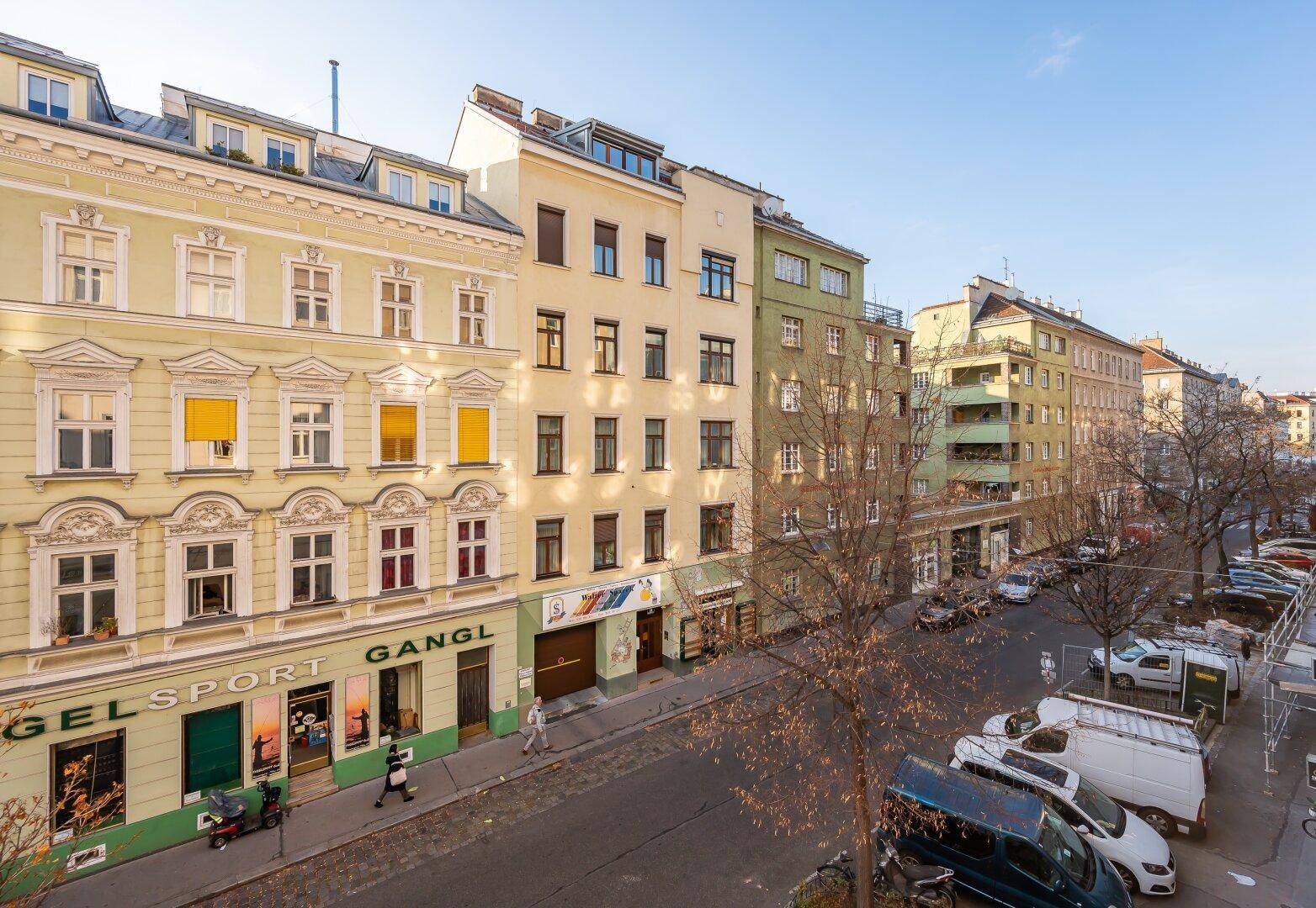 Panoramablick auf eine belebte Stadtstraße mit Altbauten und Geschäften.