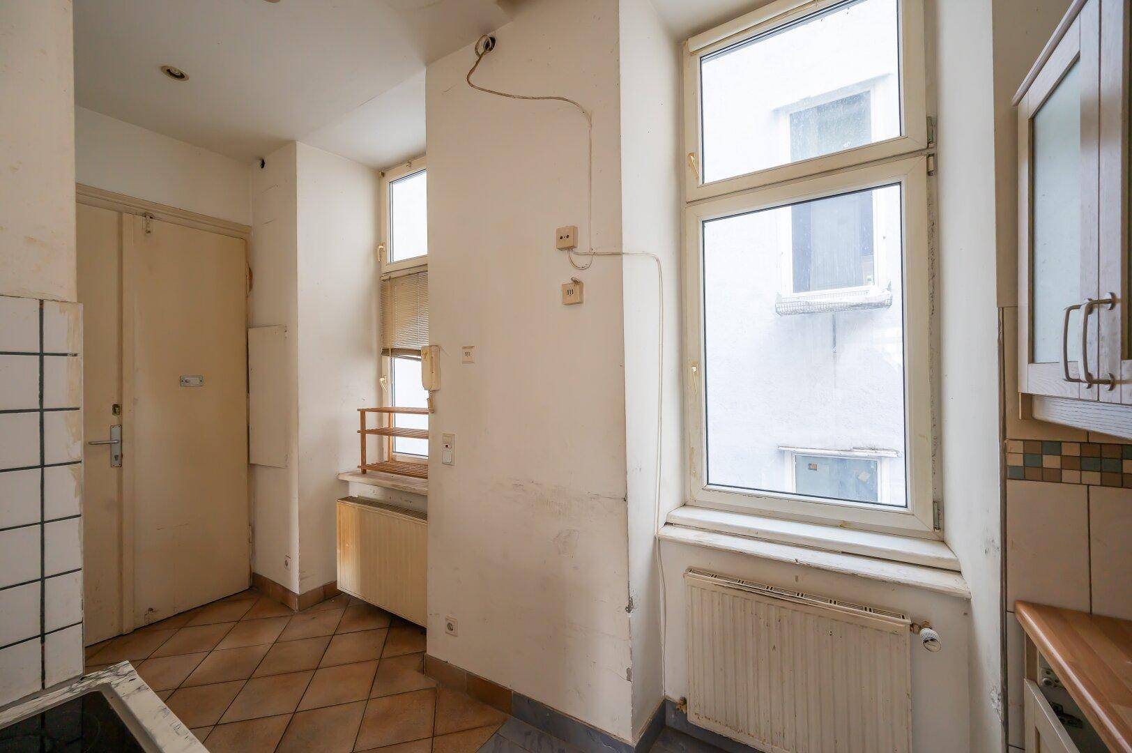 Küche mit Terrakotta-Fliesenboden und mehreren Fenstern, bereit für eine Renovierung.