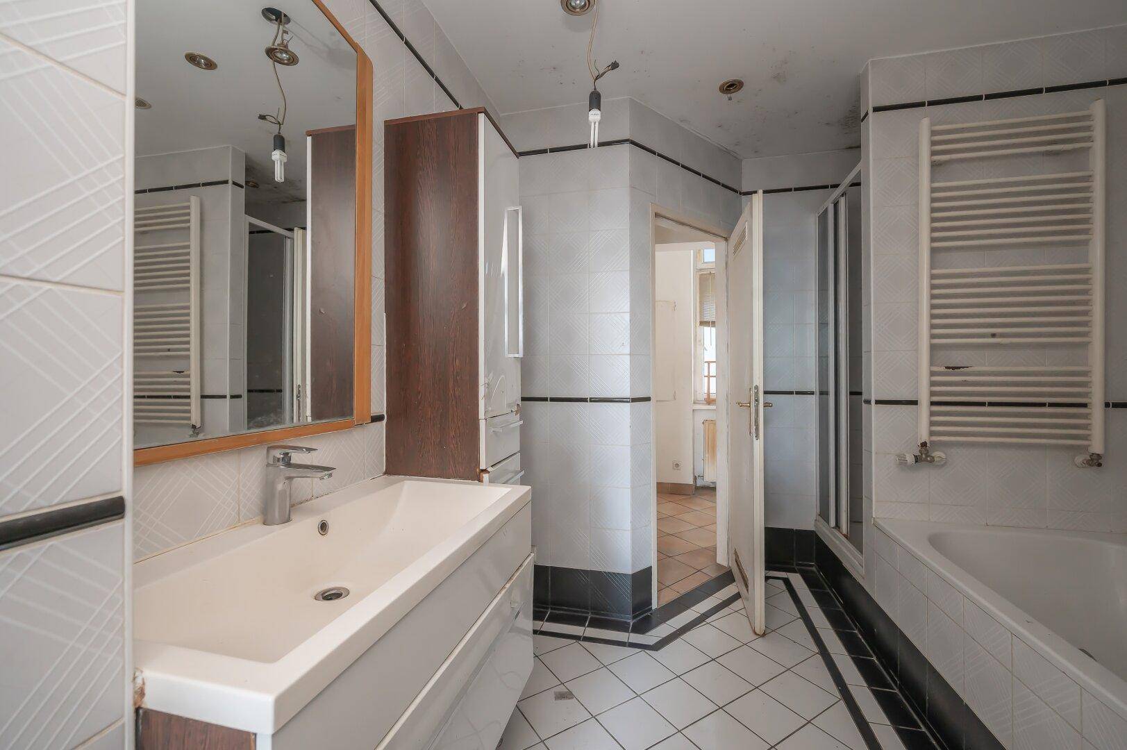 Badezimmer mit Waschbecken, Spiegel und Heizkörper, zeigt ältere Fliesen und Ausstattung.
