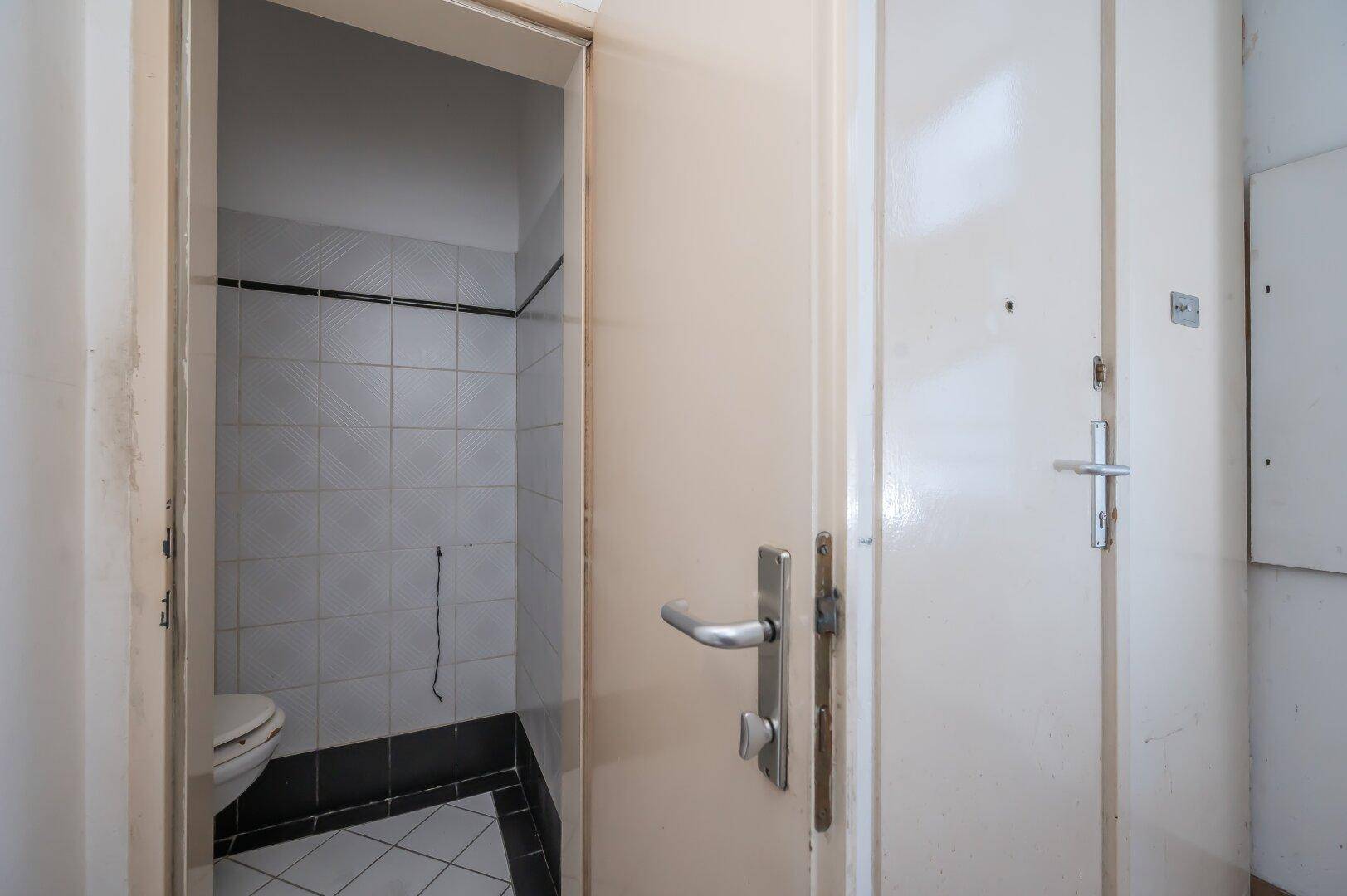 Kleines WC mit Fliesen an Wänden und Boden, direkt neben der Eingangstür.