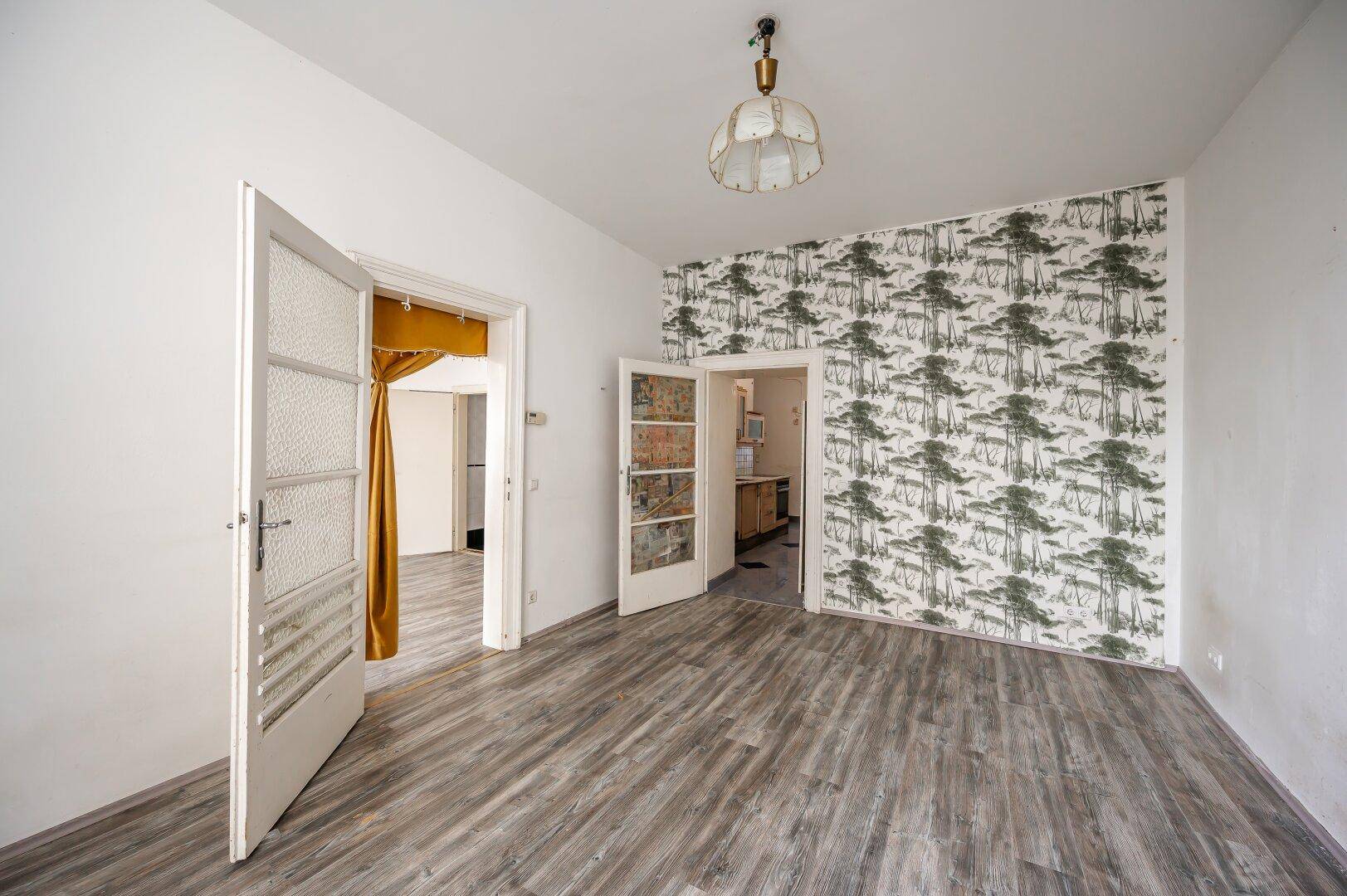 Leeres Zimmer mit Laminatboden und gemusterter Tapete, verbunden mit weiteren Räumen.