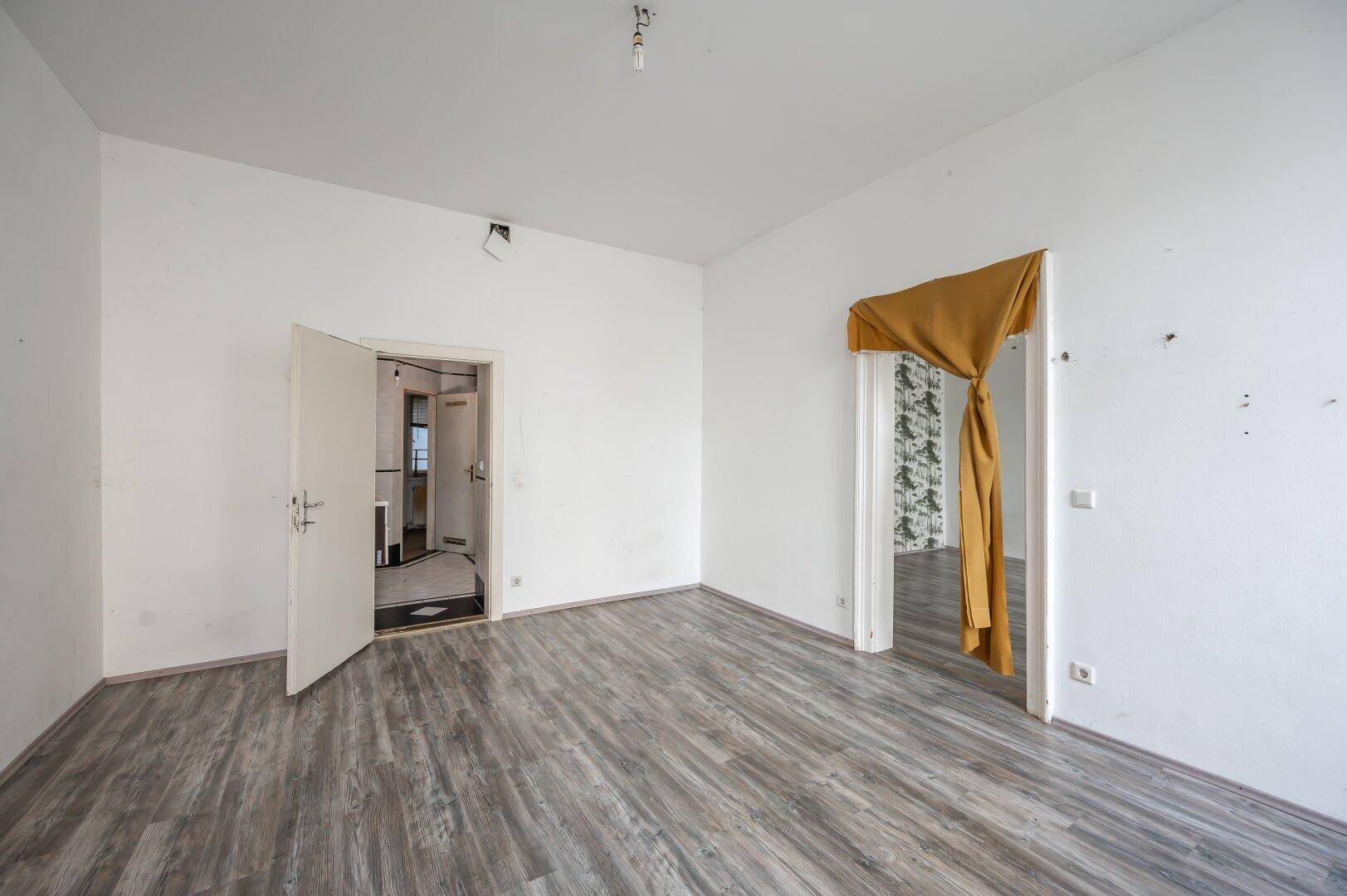 Leeres Zimmer mit Laminatboden und zwei Türen, die zu anderen Bereichen der Wohnung führen.