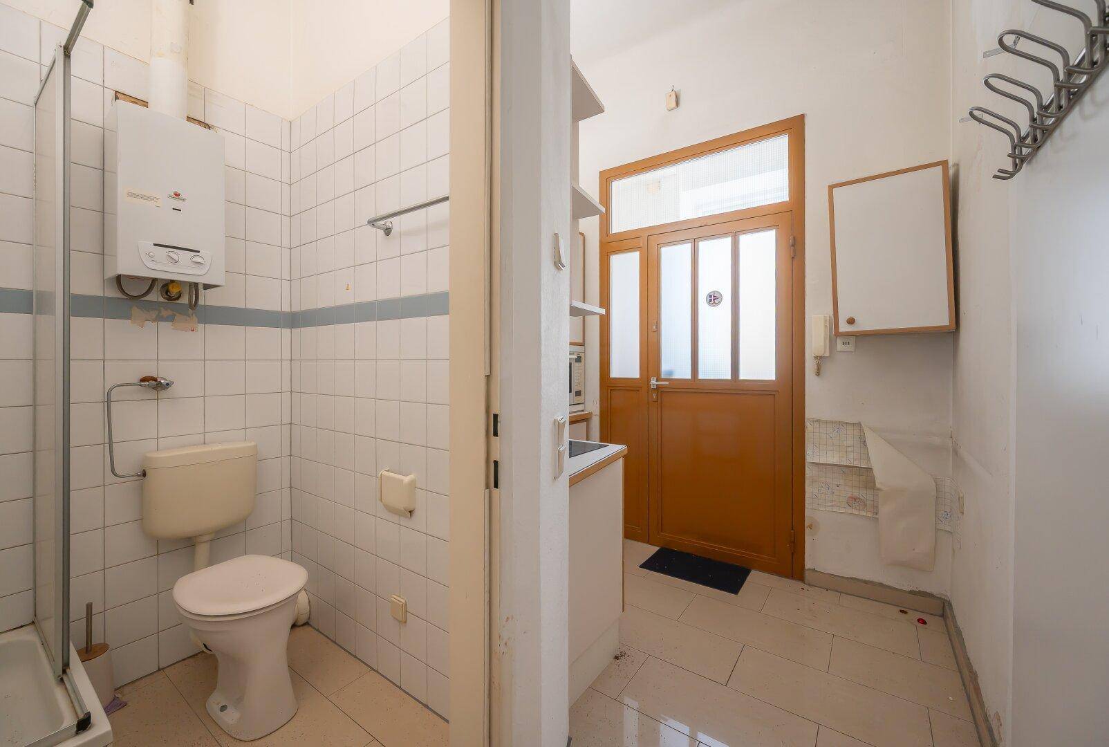 Kleines Badezimmer mit WC, Dusche und Boiler, gefliest in Weiß und Hellblau.