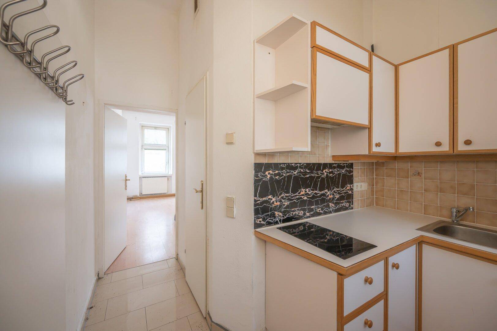 Flur mit Fliesenboden, der zu einer kleinen Küche und einem weiteren Zimmer führt.