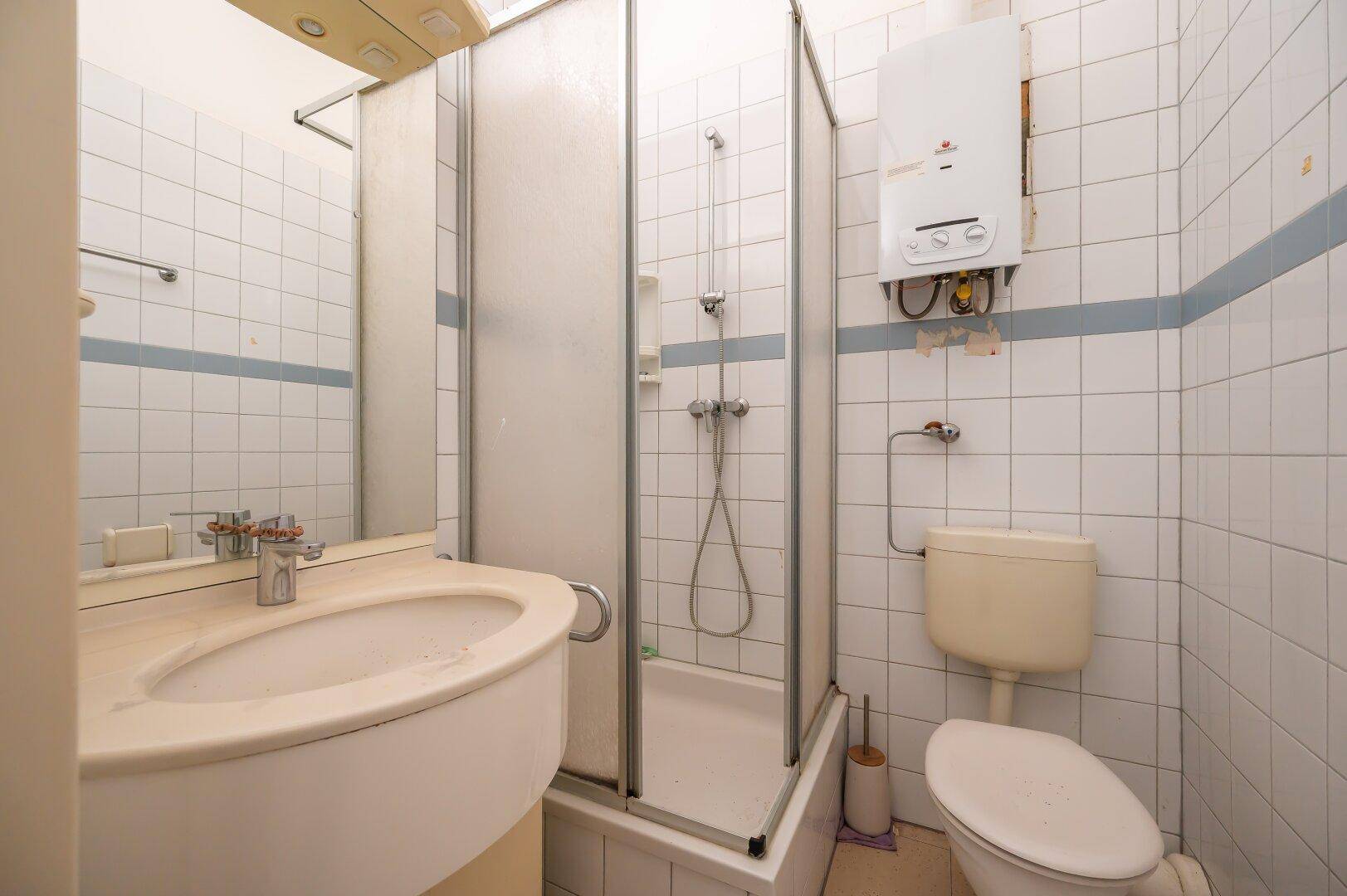Kompaktes Badezimmer mit Dusche, Waschbecken und Toilette, ausgestattet mit weißen Fliesen.