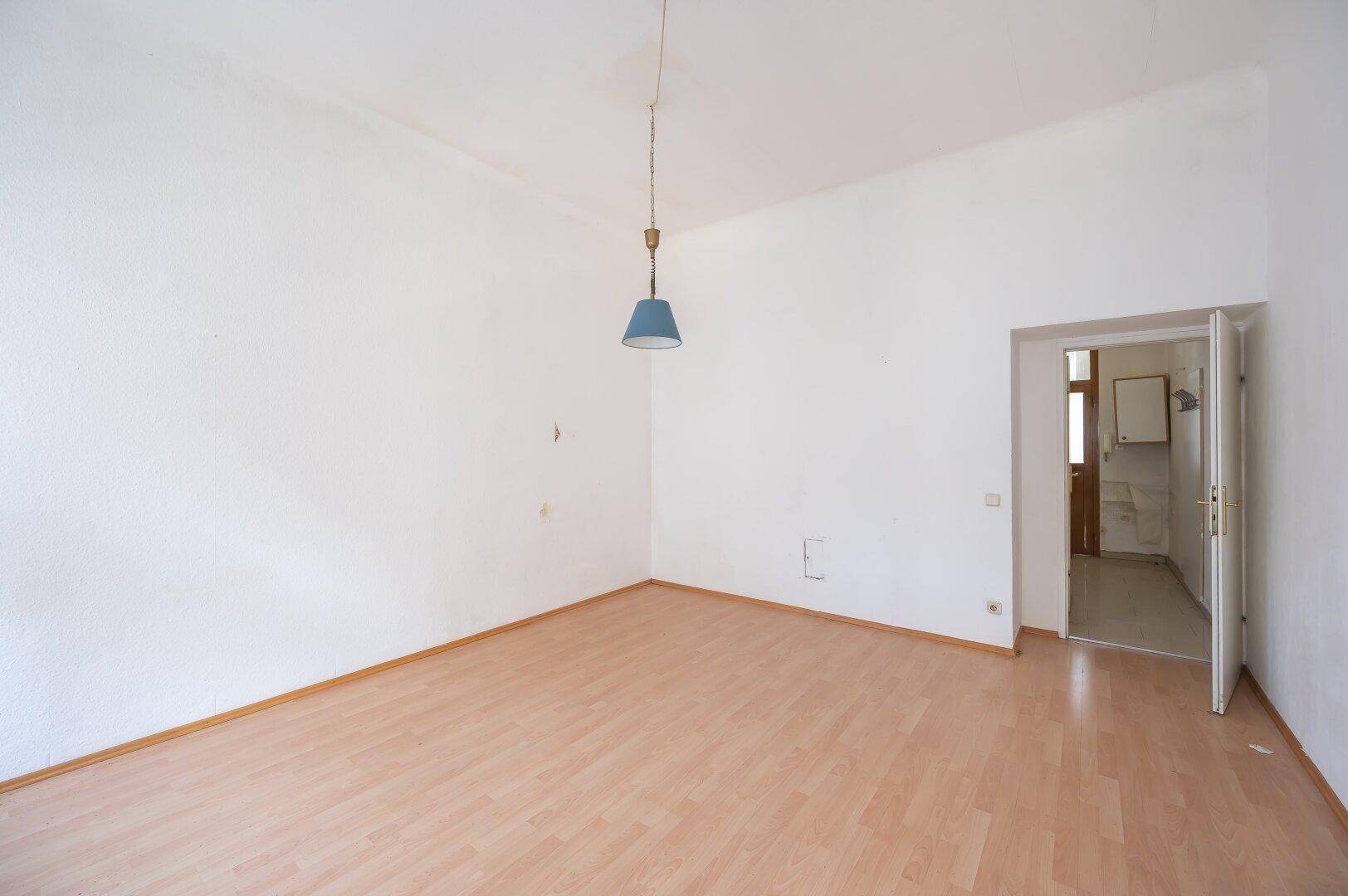 Heller, leerer Raum mit Laminatboden und einer Tür, die in einen weiteren Bereich führt.