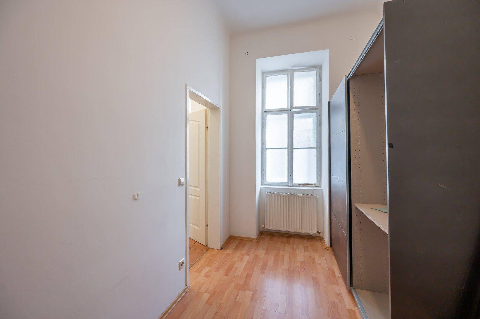 Schmaler Flur mit Laminatboden, einem Fenster und einem offenen Kleiderschrank.