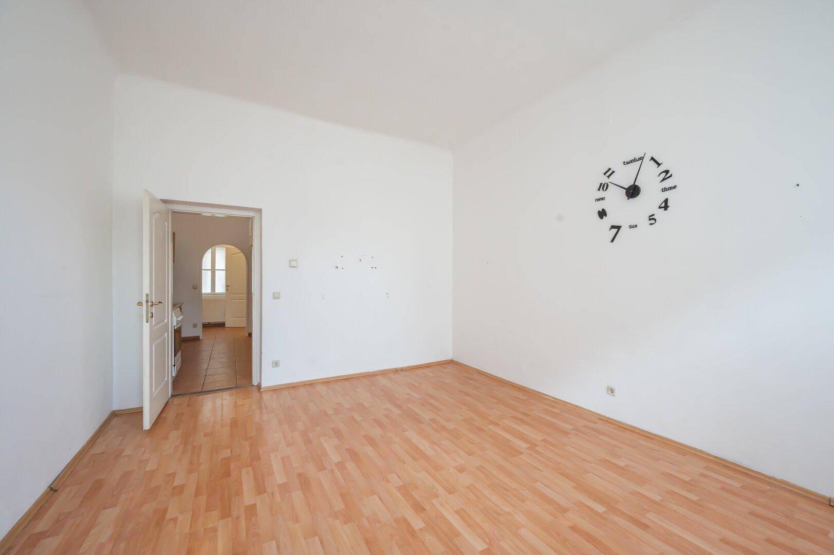 Leeres Zimmer mit Laminatboden und einer Tür, die zu einem weiteren Raum führt.