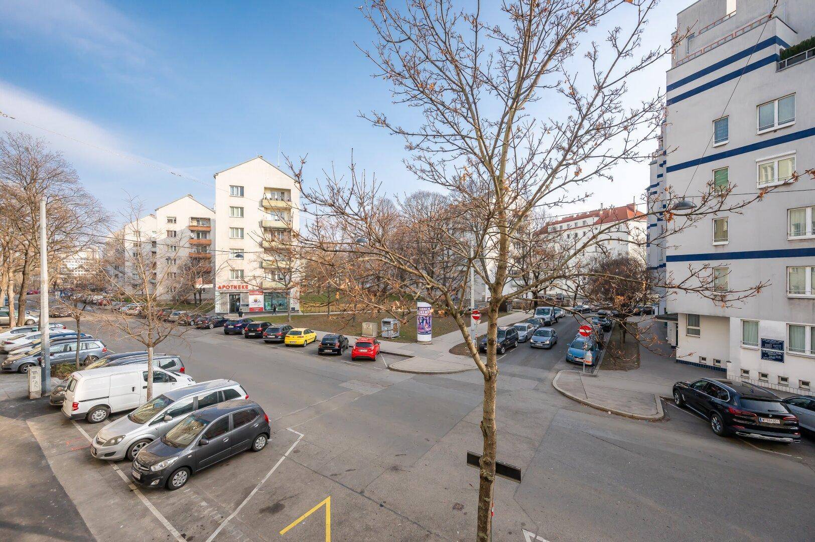 Blick auf eine städtische Straße mit parkenden Autos und Wohngebäuden unter blauem Himmel.