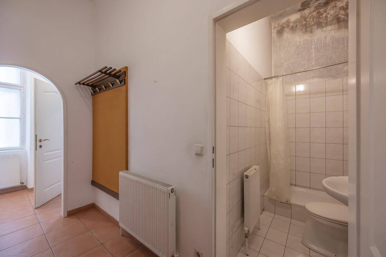 Flur mit Fliesenboden und Zugang zu einem kleinen Badezimmer mit Duschbereich.