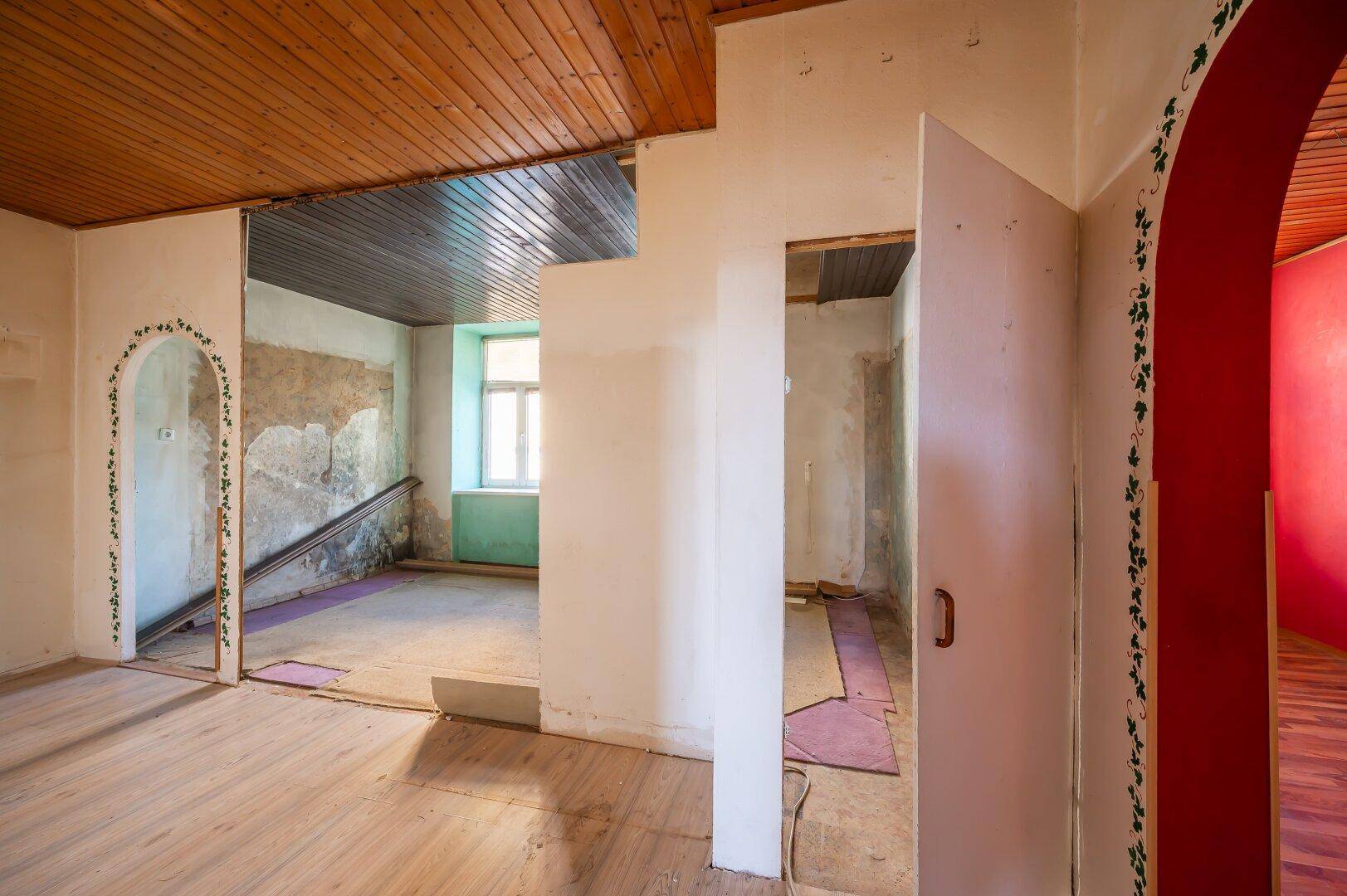 Renovierungsbedürftiger Innenraum mit Holzbalkendecke und teilweise freigelegten Wänden, bietet Gestaltungsmöglichkeiten.