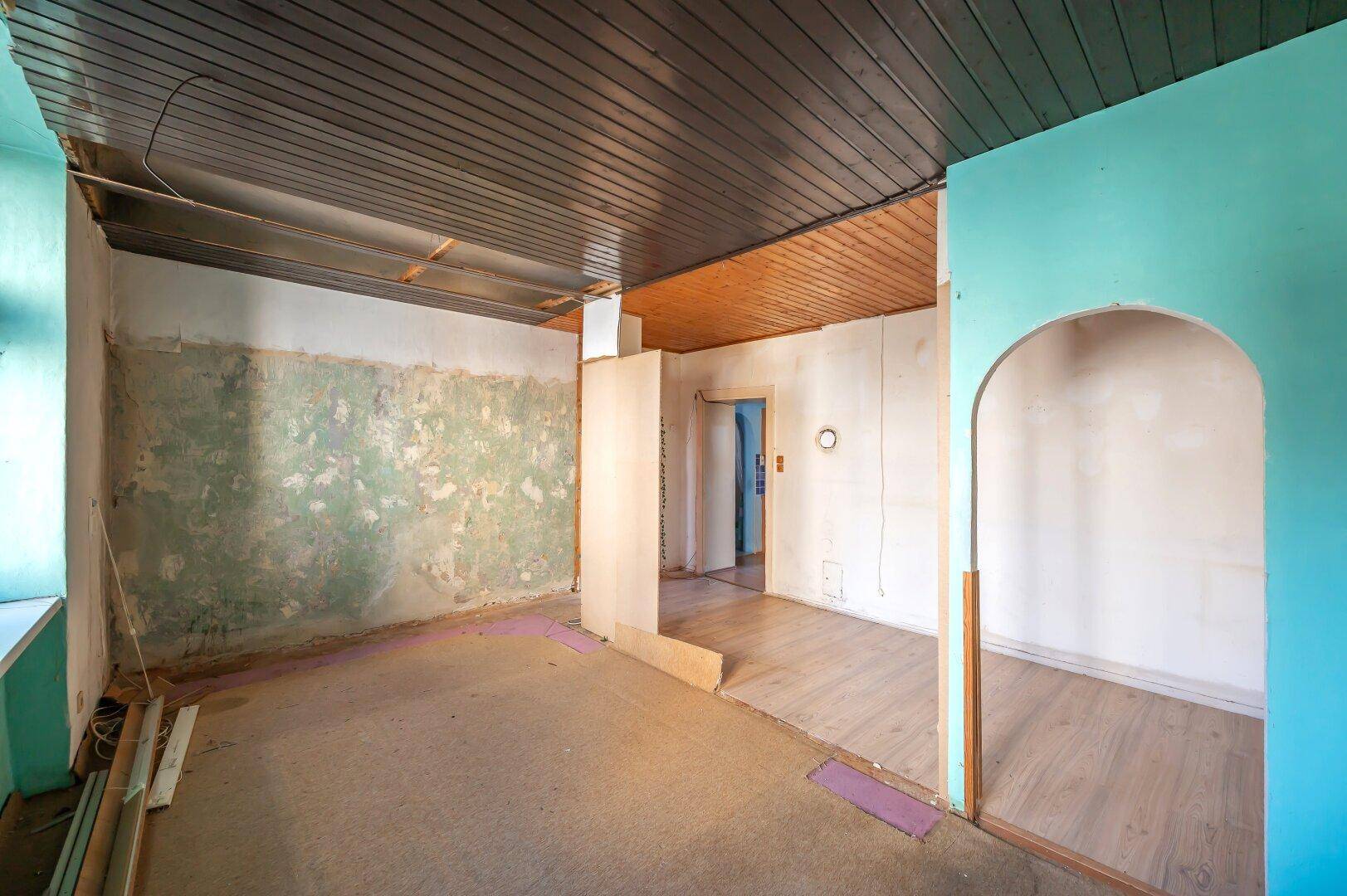 Renovierungsbedürftiger Raum mit Holzbalkendecke und sichtbaren Spuren früherer Wandgestaltung.