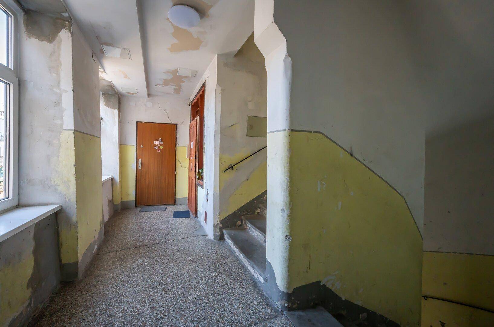 Treppenhaus eines Altbaus mit abgenutzten Wänden und Terrazzoboden, benötigt Renovierung.