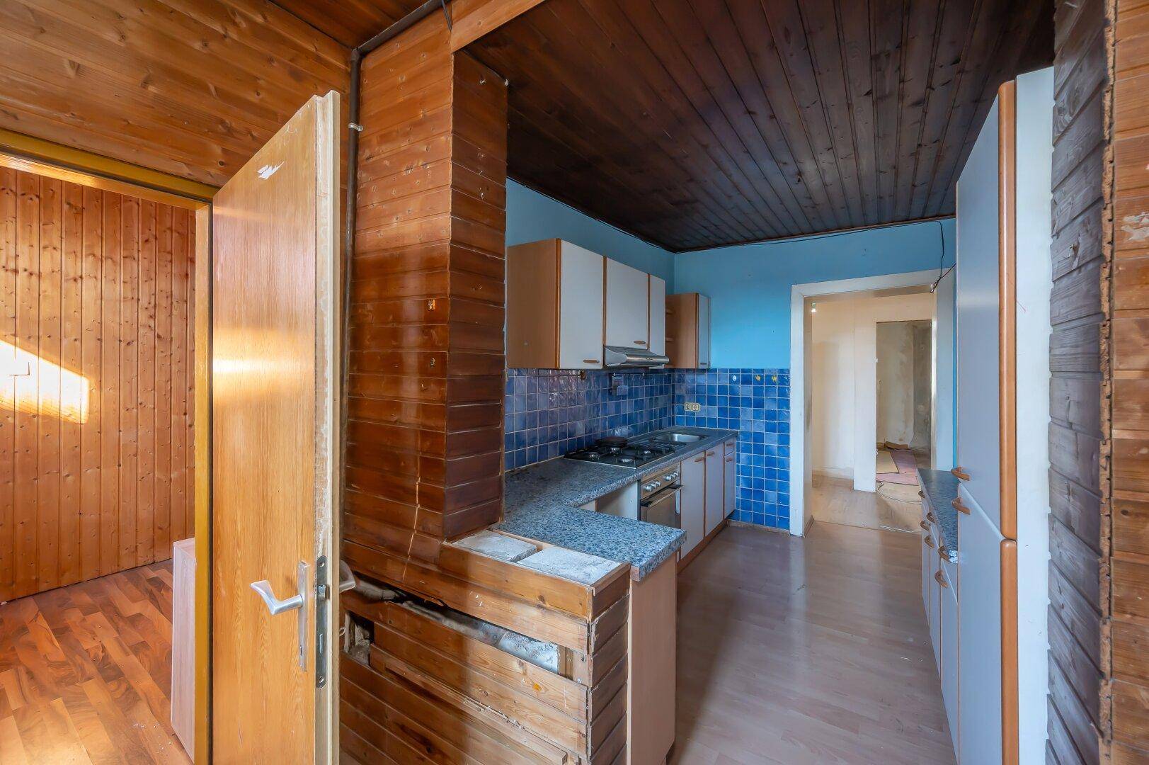 Küche mit blauen Wandfliesen, Holzvertäfelung und älteren Einbauschränken, bietet Renovierungspotenzial.