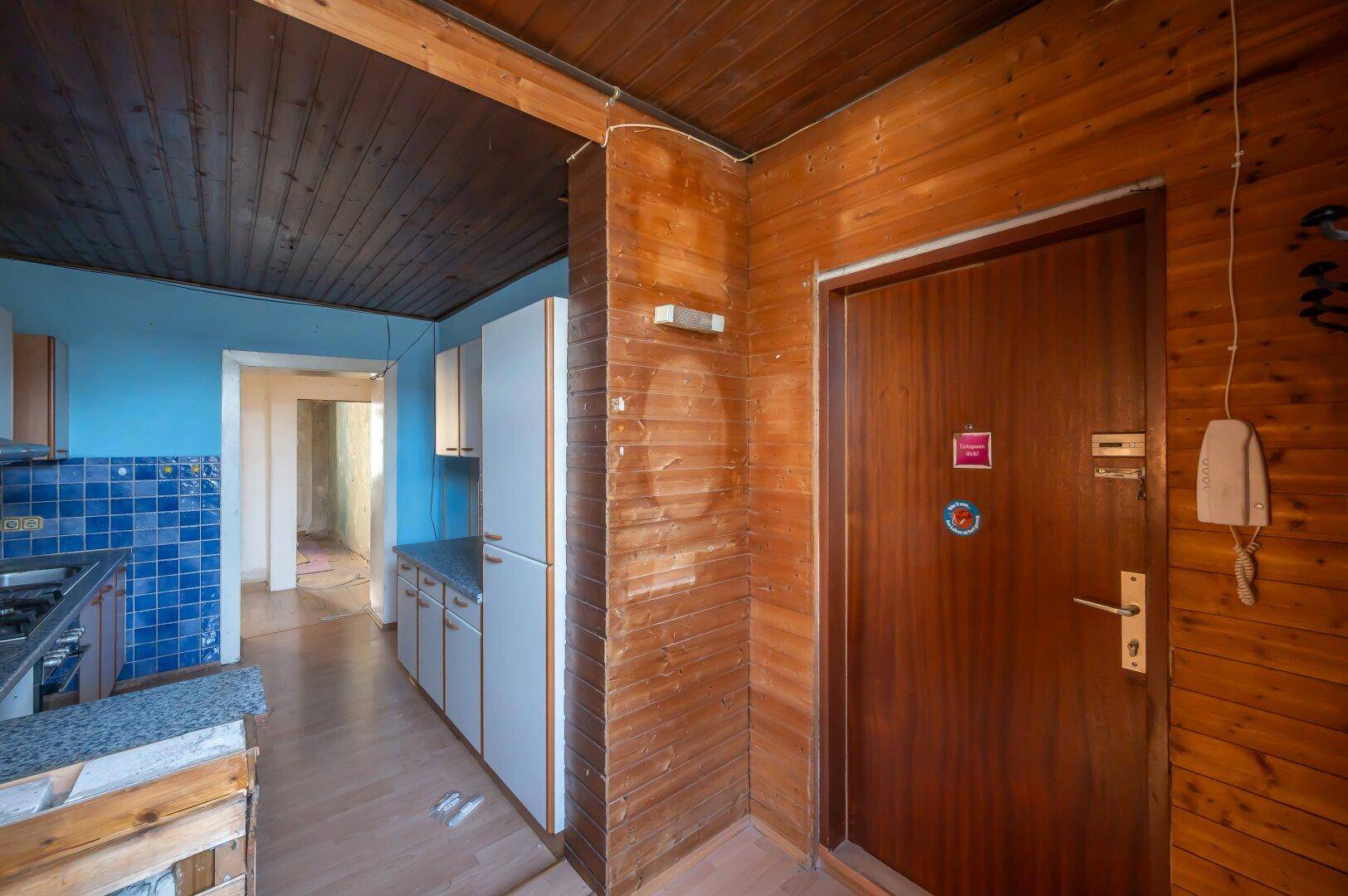 Eingangsbereich mit Holzvertäfelung und Blick in die angrenzende Küche, benötigt Modernisierung.