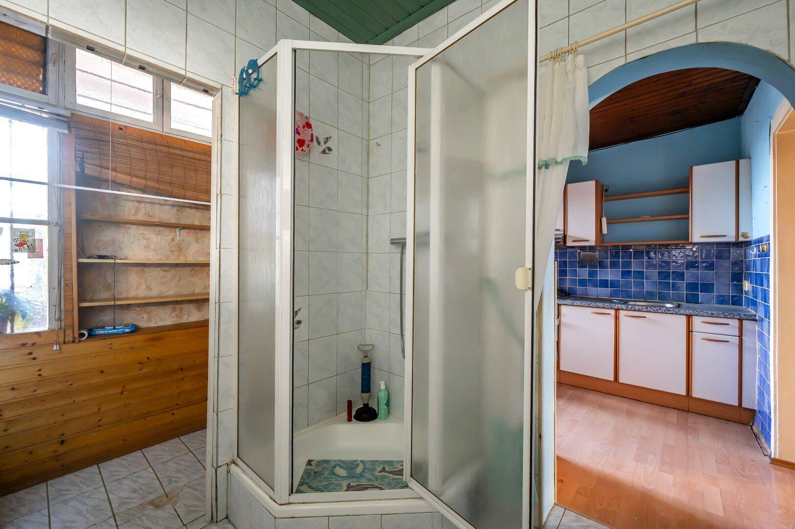 Badezimmer mit Duschkabine und Fliesenboden, bietet direkten Zugang zur Küche.