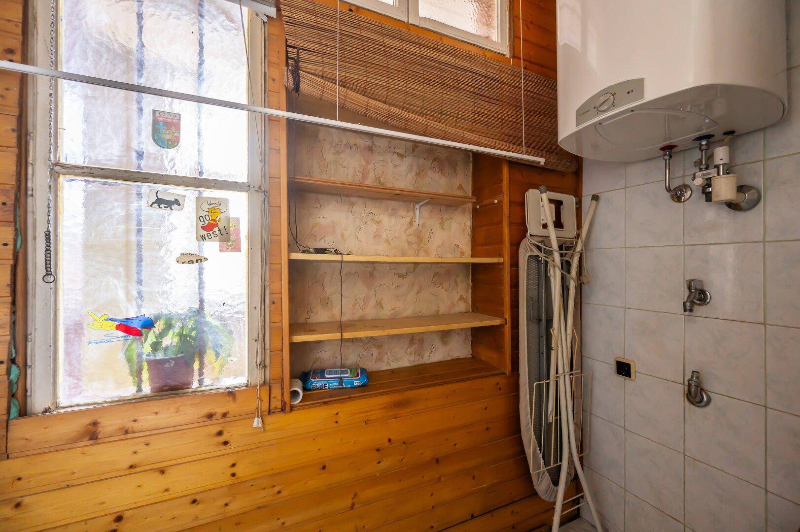 Hauswirtschaftsraum mit Warmwasserboiler, Regalen und Bügelbrett, bietet praktischen Stauraum.