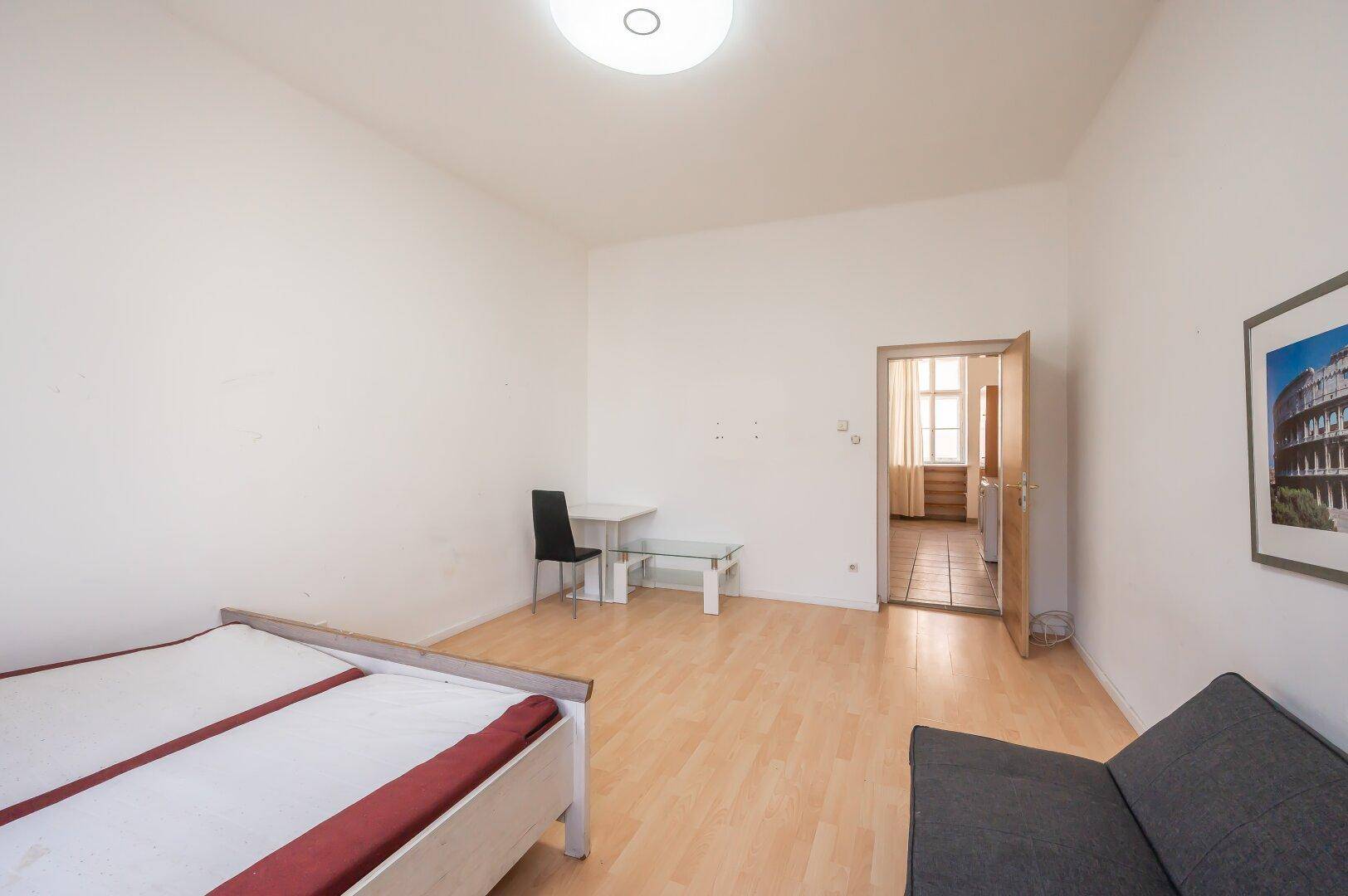 Geräumiges Schlafzimmer mit Parkettboden, kleinem Tisch und Zugang zu einem weiteren Raum.