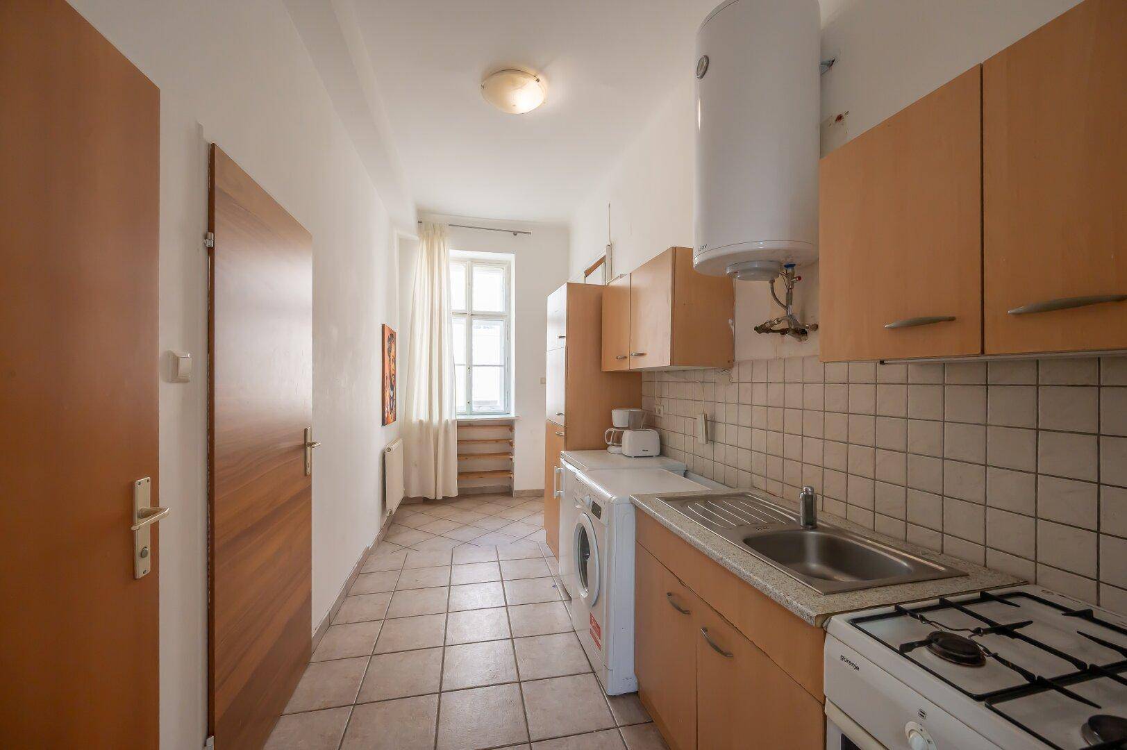 Funktionale Küche mit hellen Holzschränken, Gasherd, Spüle und Waschmaschine, gut beleuchtet.