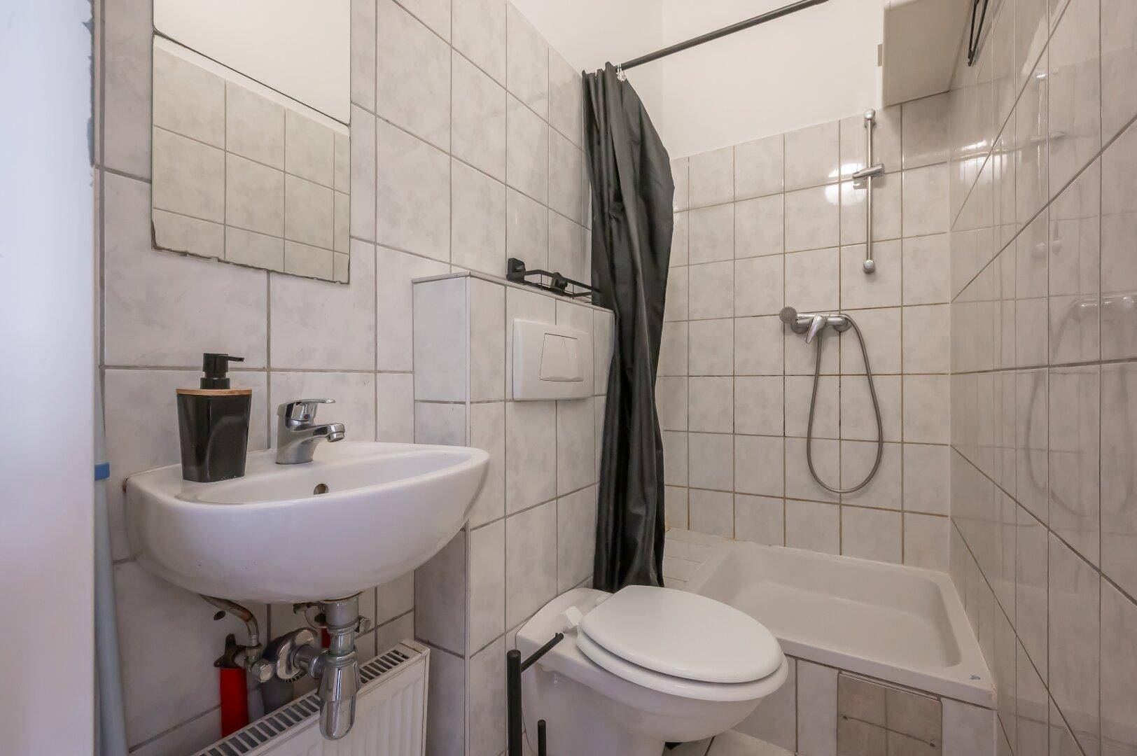Gefliestes Badezimmer mit Waschbecken, Toilette und Badewanne mit Duschvorhang.