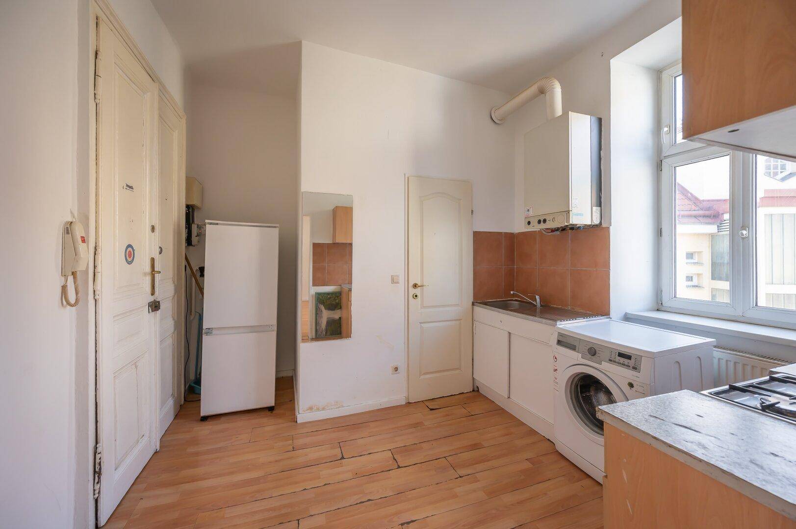 Einfache Küche mit Waschmaschine, Kühlschrank und Gastherme, bereit zur Einrichtung.