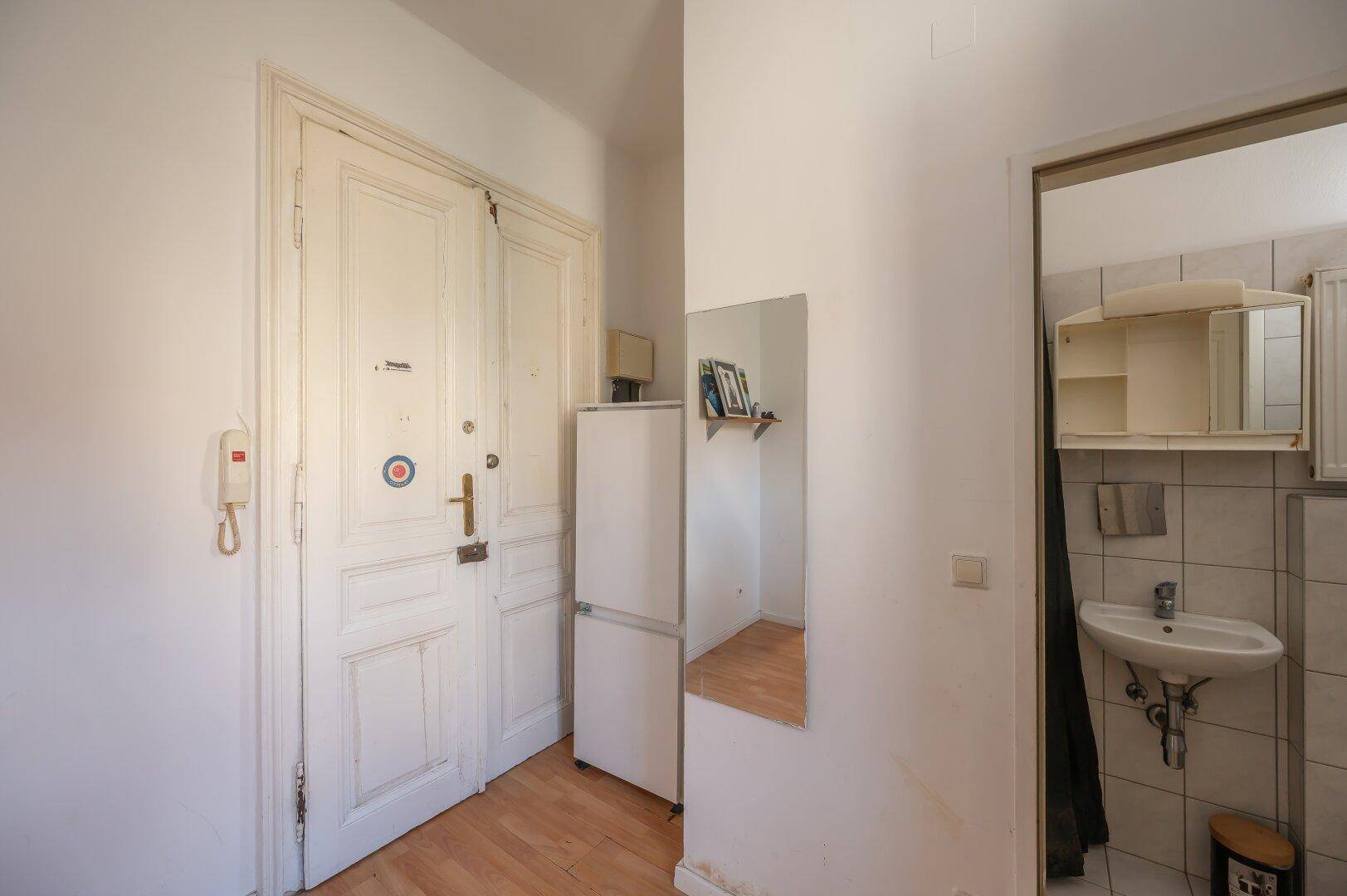 Eingangsbereich mit alter Holztür, Kühlschrank und Spiegel, führt zur Küche.