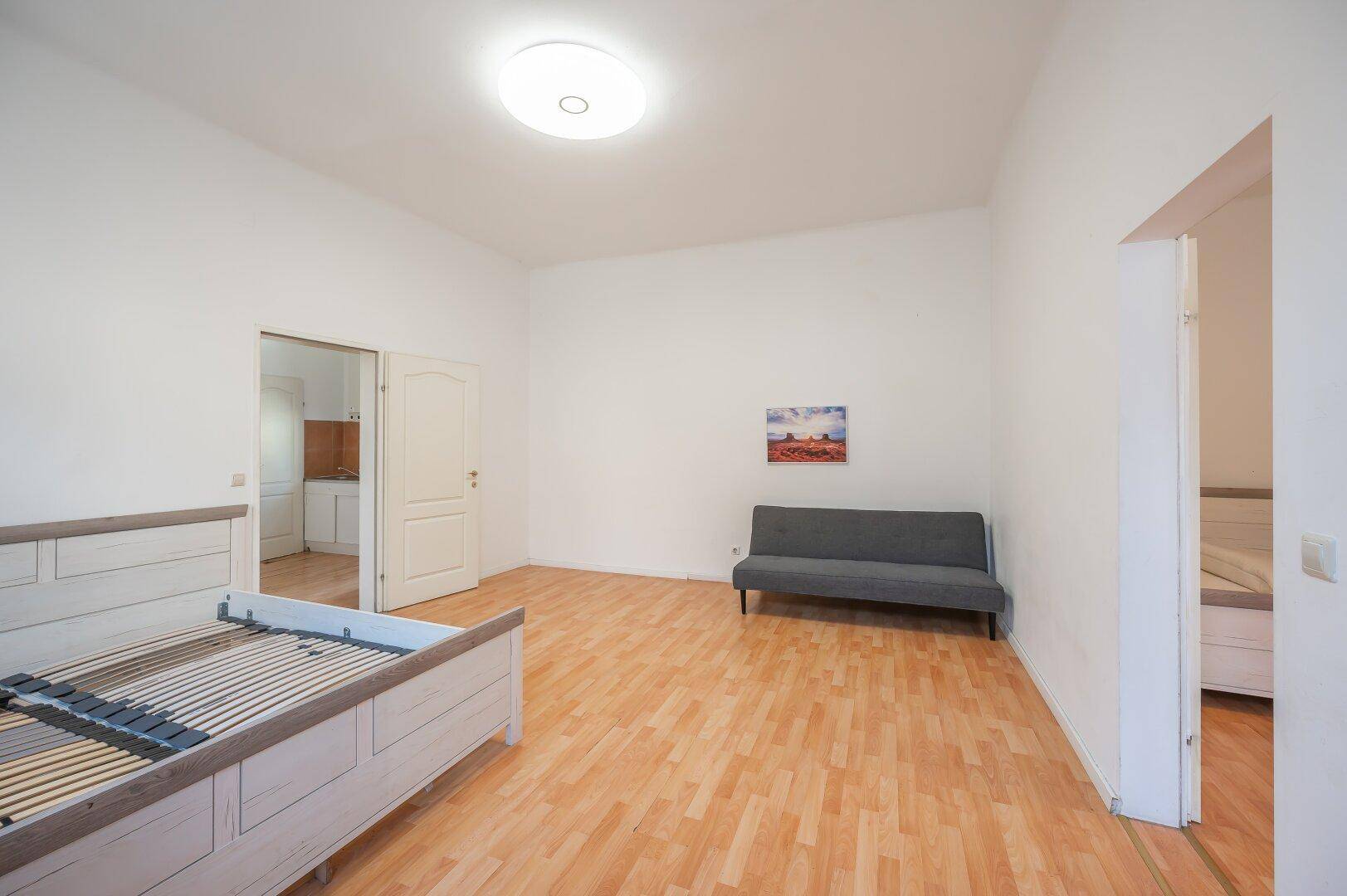 Geräumiges Schlafzimmer mit Holzboden, einem Sofa und Zugang zu weiteren Räumen.
