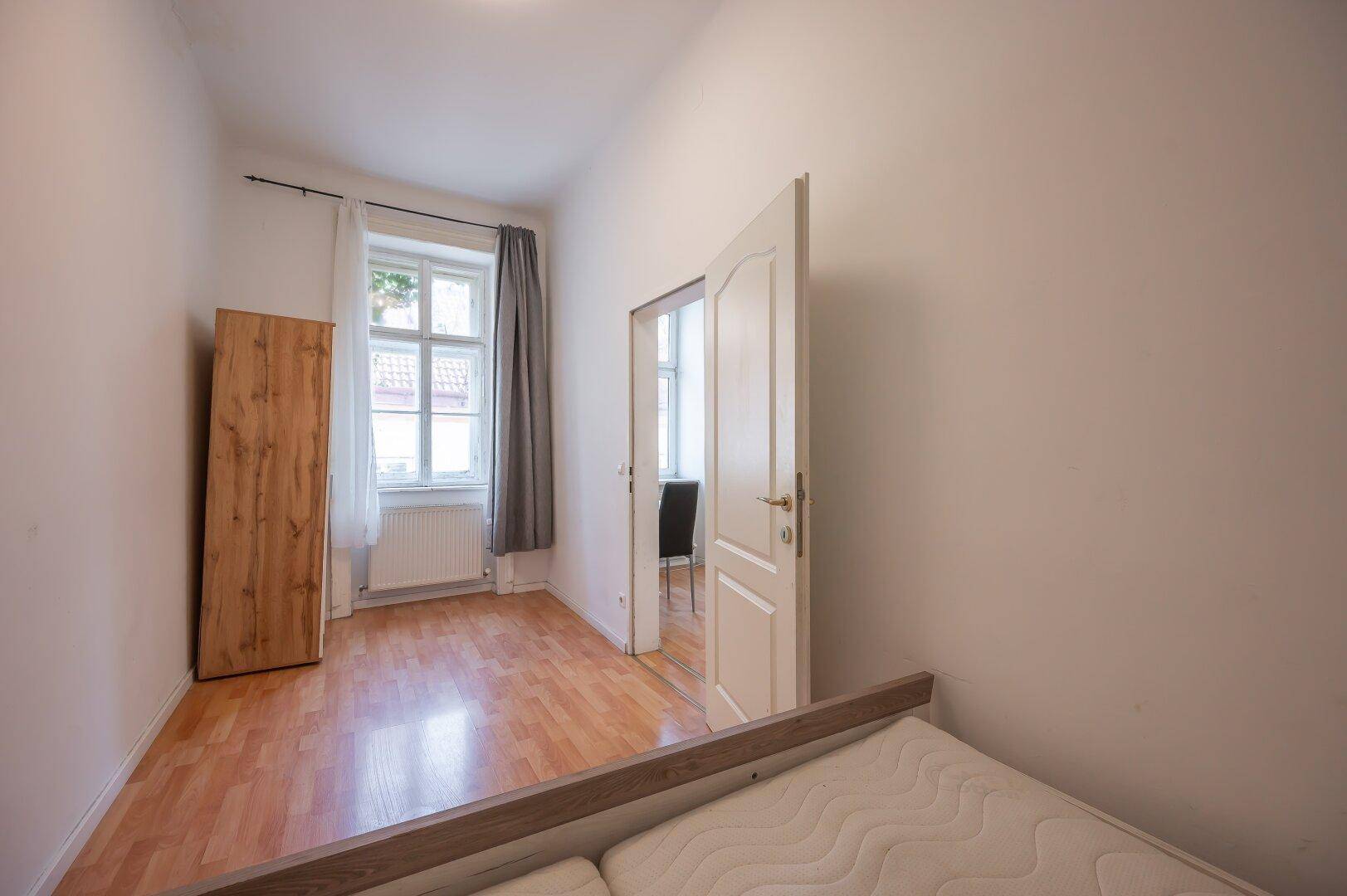Kleineres Schlafzimmer mit Holzboden, einem Fenster und einem Holzschrank.